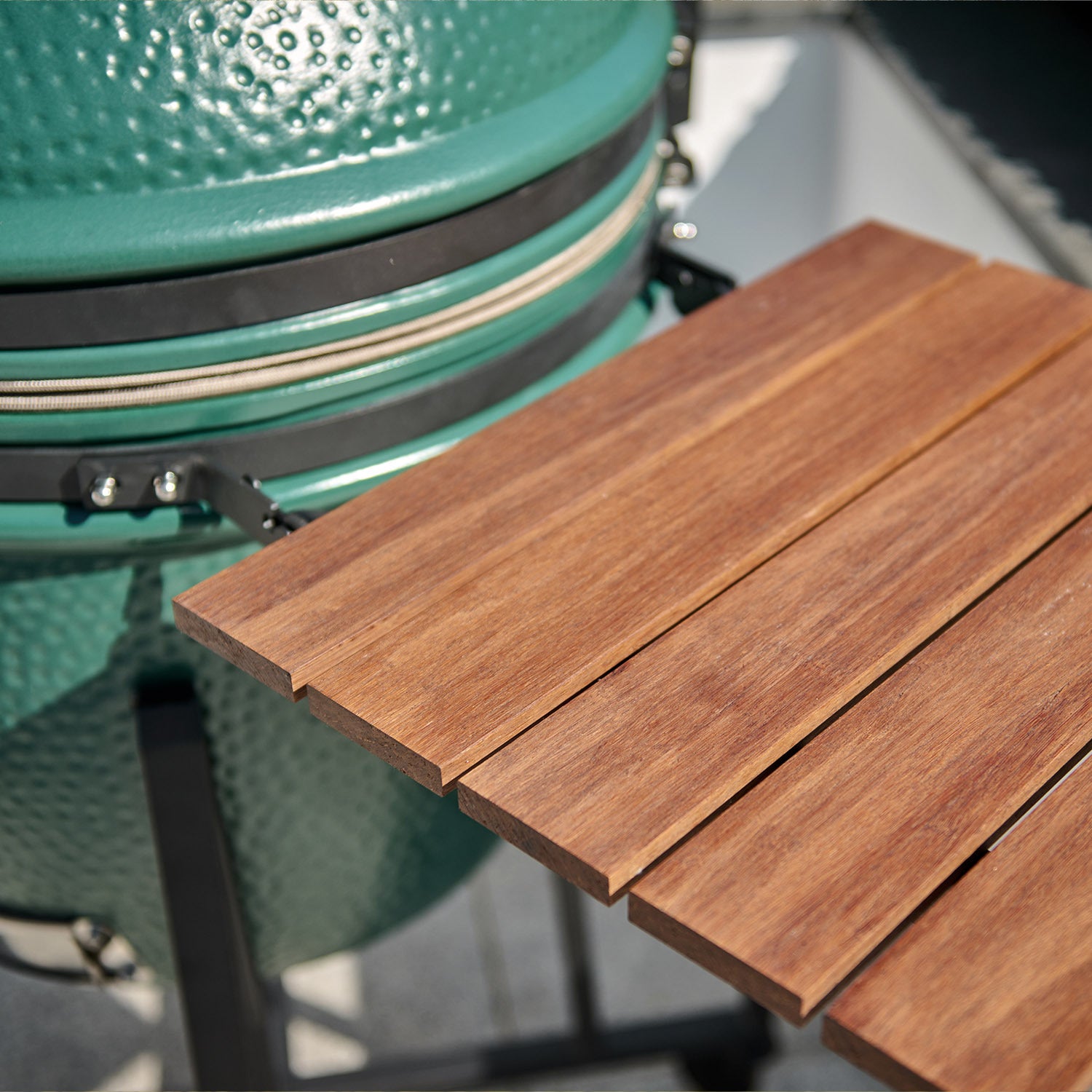 Close-up of the Kamado BBQ 22" Ceramic Grill in Matte Green with a wooden side shelf on a sunny day.