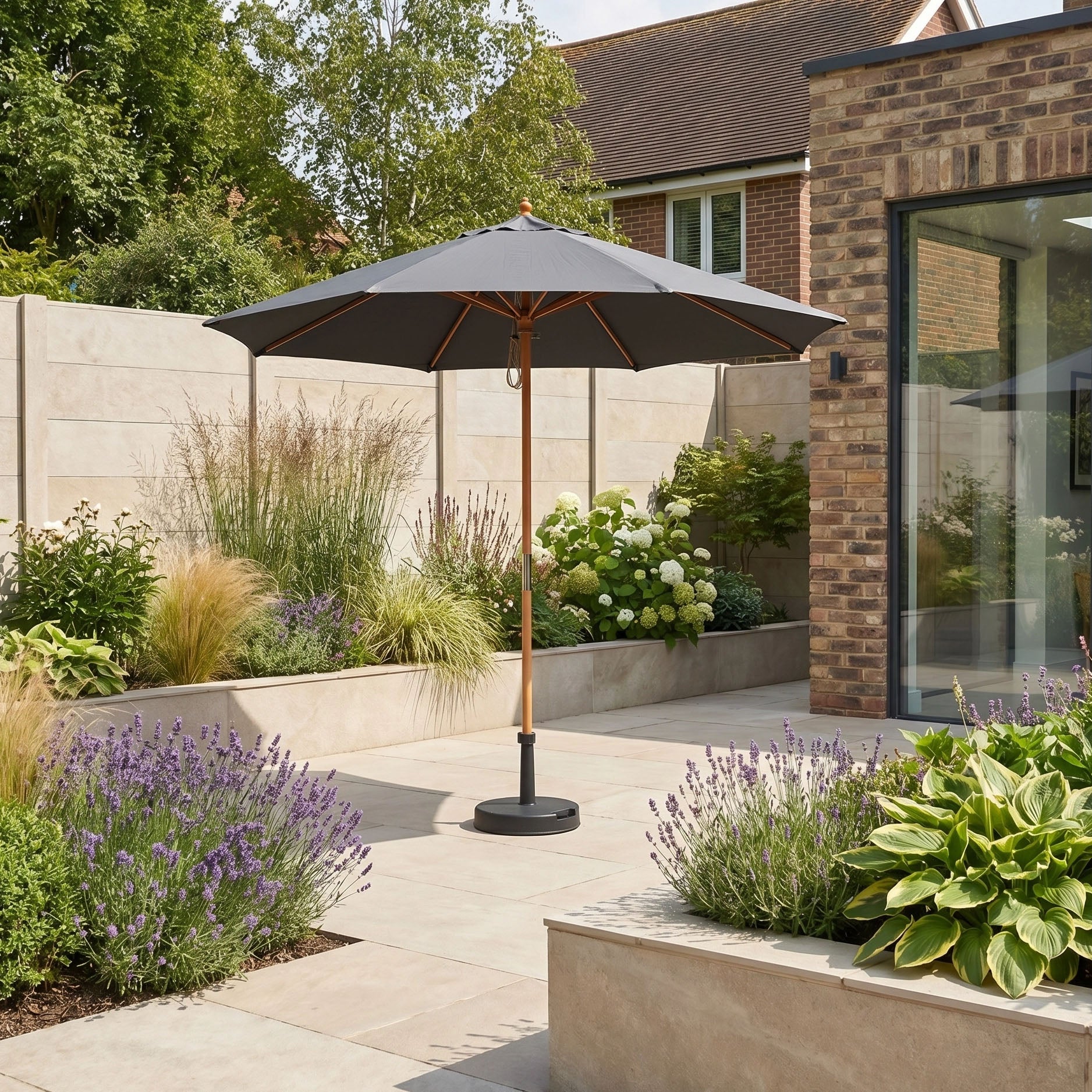 A patio garden with greenery, purple flowers, and the Kratos 2.5m Round Wooden Parasol in Grey (UV 50+) at the center.