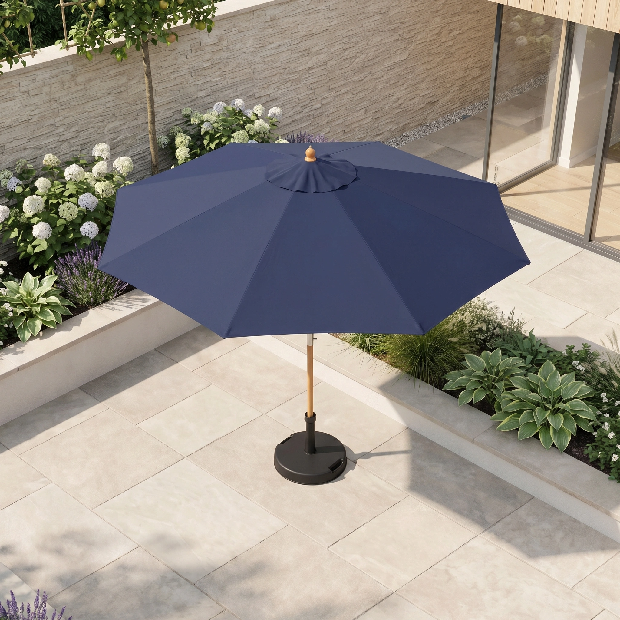 The Kratos 2.5m Round Wooden Parasol in Navy stands open on a tiled terrace, surrounded by lush green plants and blooming white flowers.