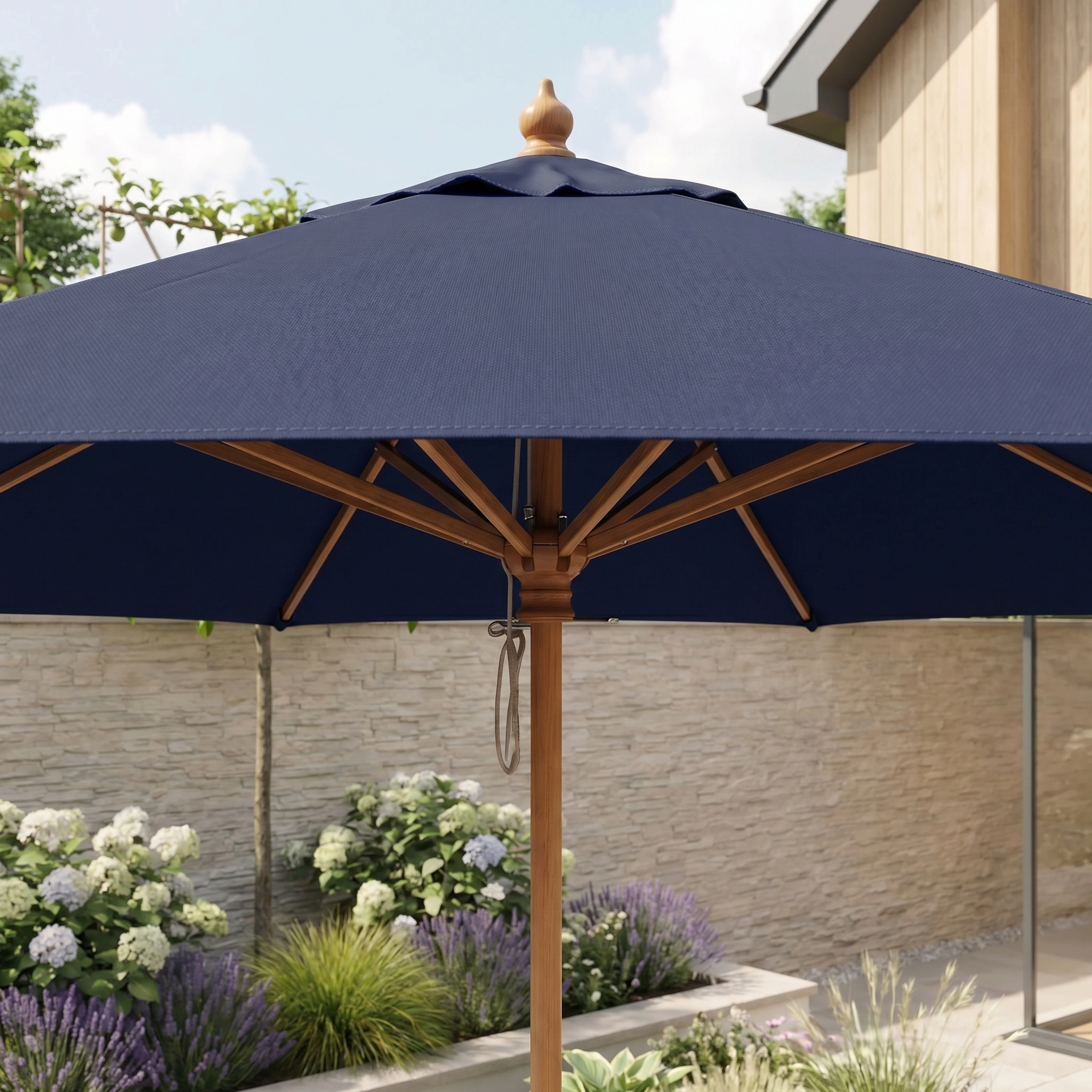 The Kratos 2.5m Round Wooden Parasol in Navy stands open in a sunny garden with flowers and a stone wall, bringing both style and shade to your outdoor space.