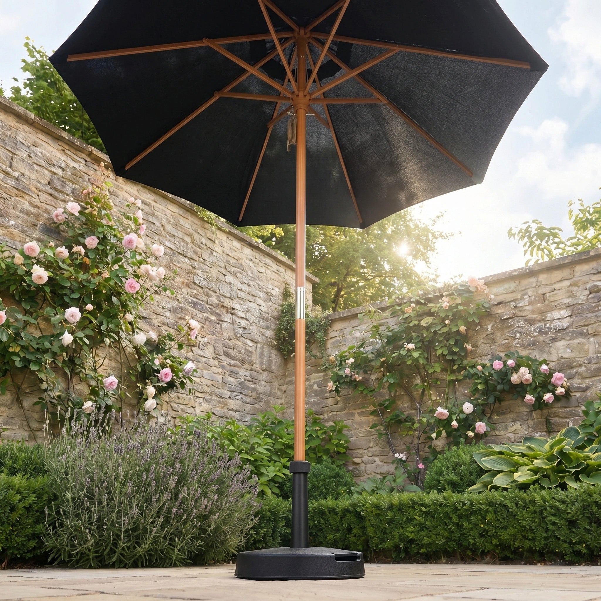The Kratos 2m Round Wooden Parasol in Black adds stylish shade to sunny gardens with stone walls, blooming roses, and lush greenery.