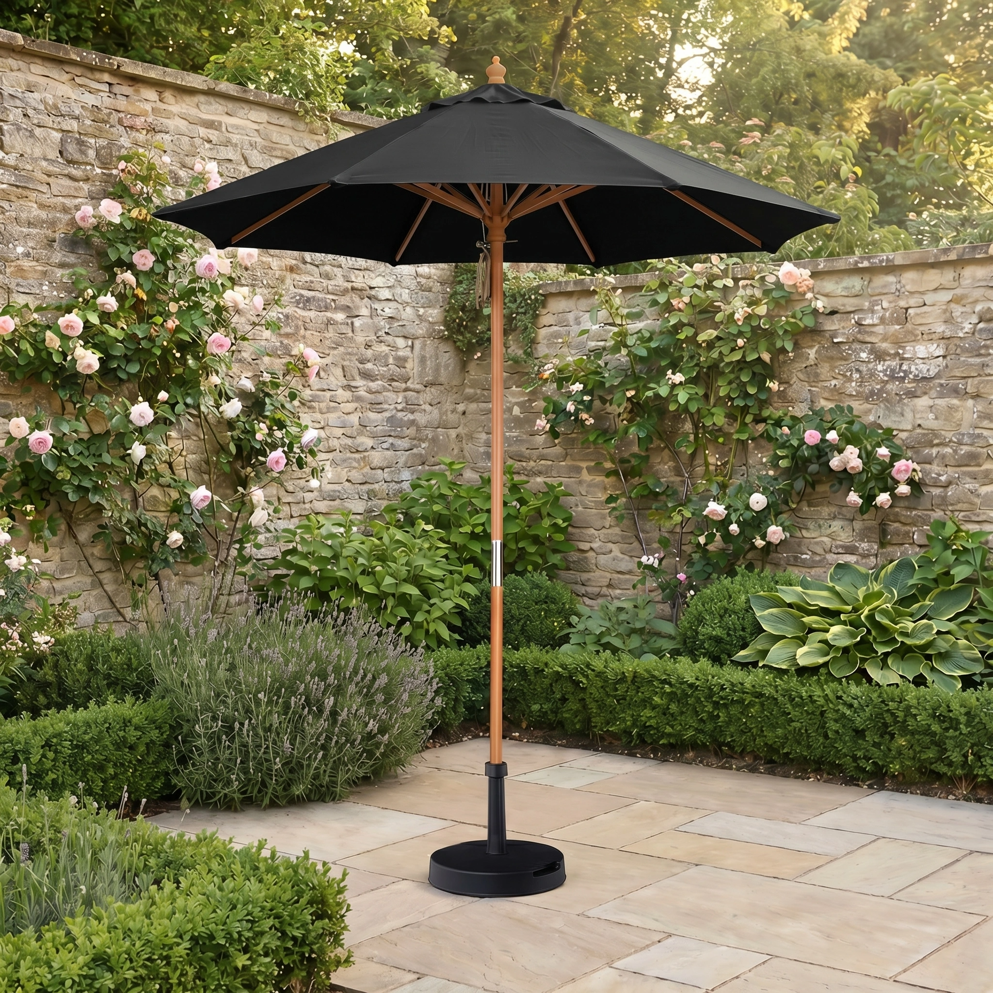 The Kratos 2m Round Wooden Parasol in Black stands in a stone-paved garden among blooming roses, providing elegance and UV protection to your outdoor space.