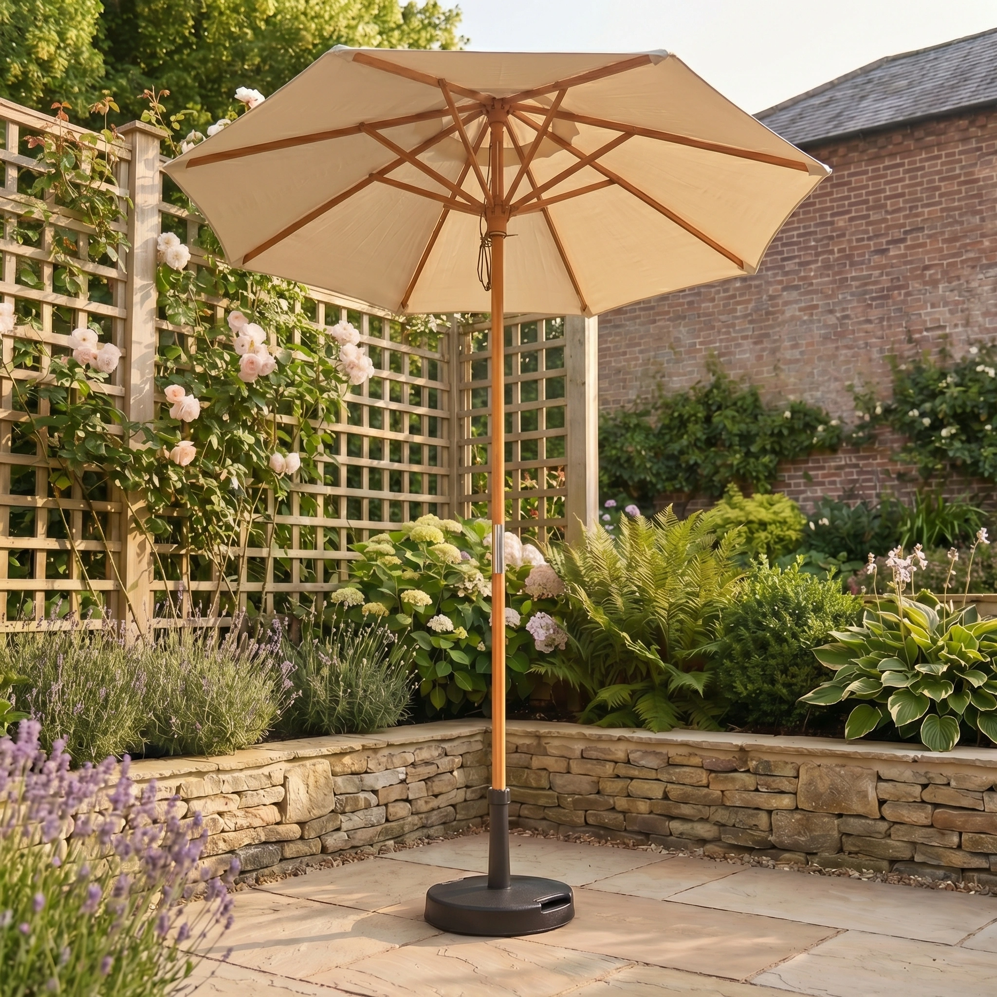 The Kratos 2m Round Wooden Parasol in Beige, featuring UV 50+ protection, stands on a stone patio amidst flowers and greenery in a garden.