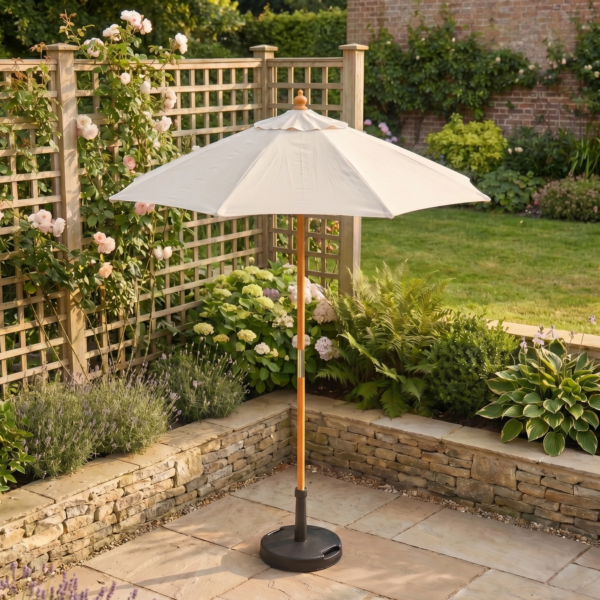 The Kratos 2m Round Wooden Parasol in Beige stands on a stone patio amidst flowering plants, lush greenery, and a wooden trellis. It features UV 50+ sun protection and a durable white wood frame.