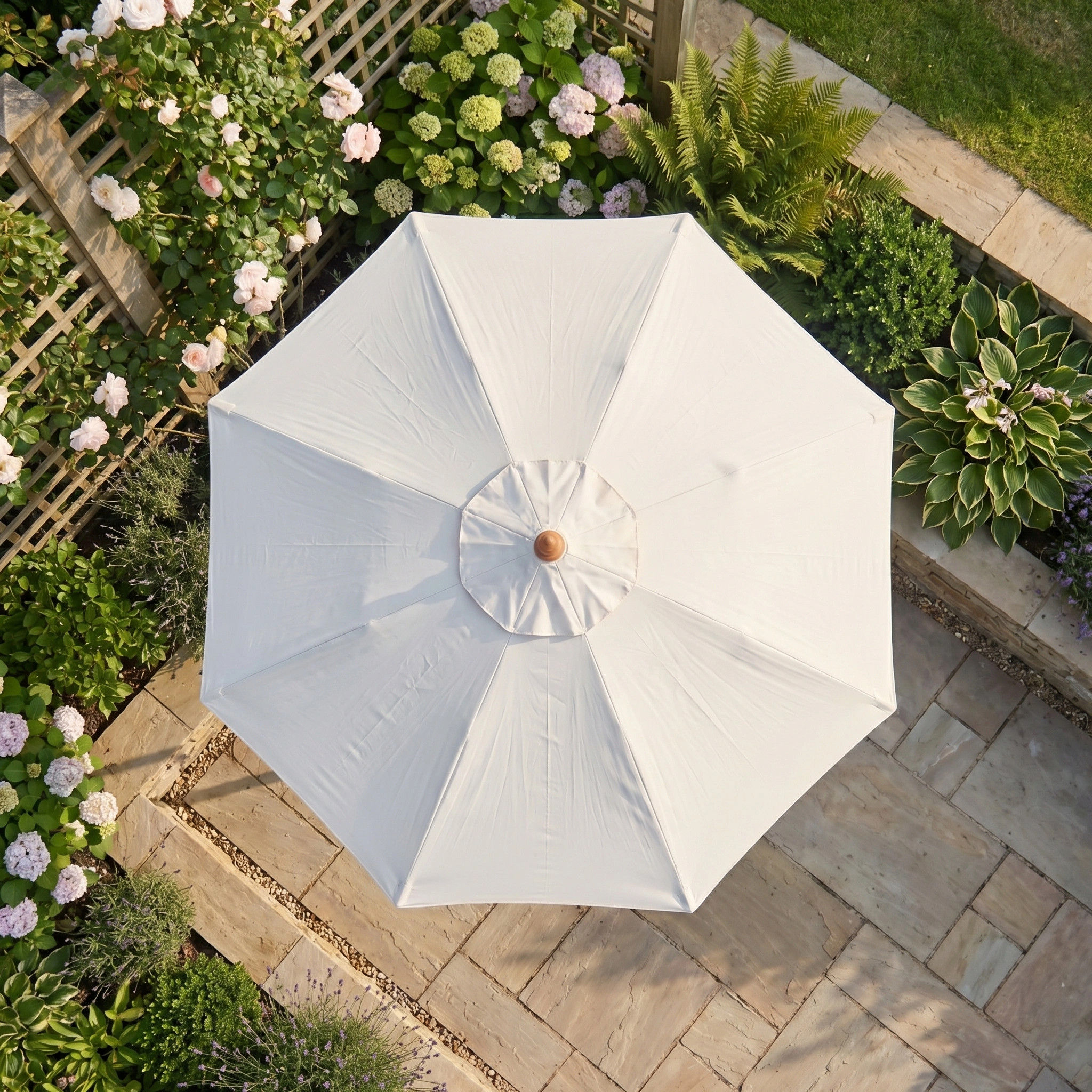 The Kratos 2m Round Wooden Parasol in Beige offers sun protection, seen from above against stone paving and vibrant garden greenery.