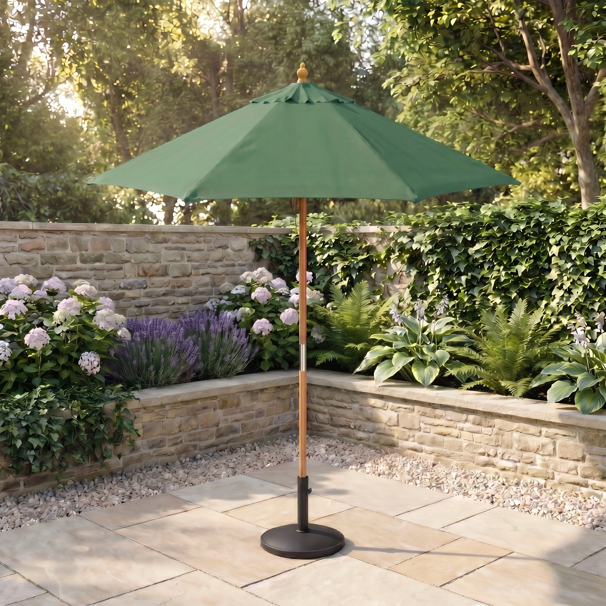 The Kratos 2m Round Wooden Parasol in Green with UV 50+ stands on stone tiles in a garden featuring flowers, shrubs, and a stone wall.