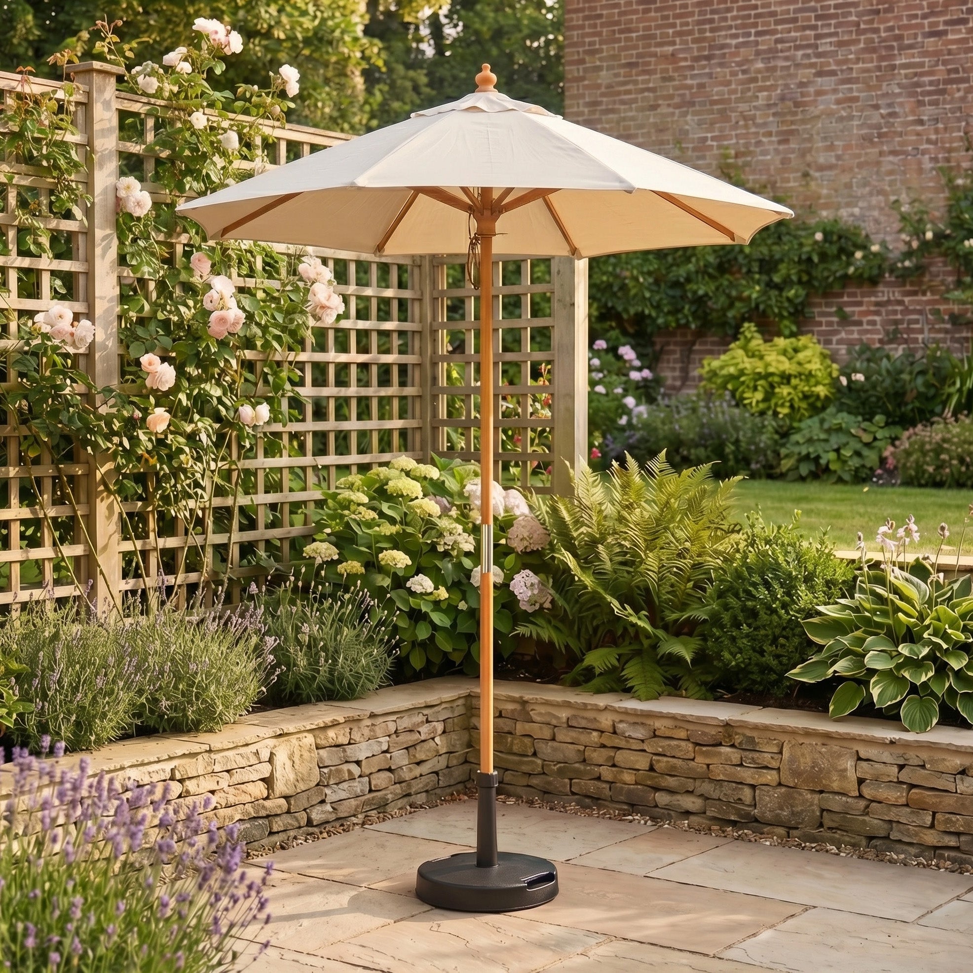 The Kratos 2m Round Wooden Parasol in Beige, UV 50+ rated, stands on a stone patio amid flowers, shrubs, and a wooden trellis.