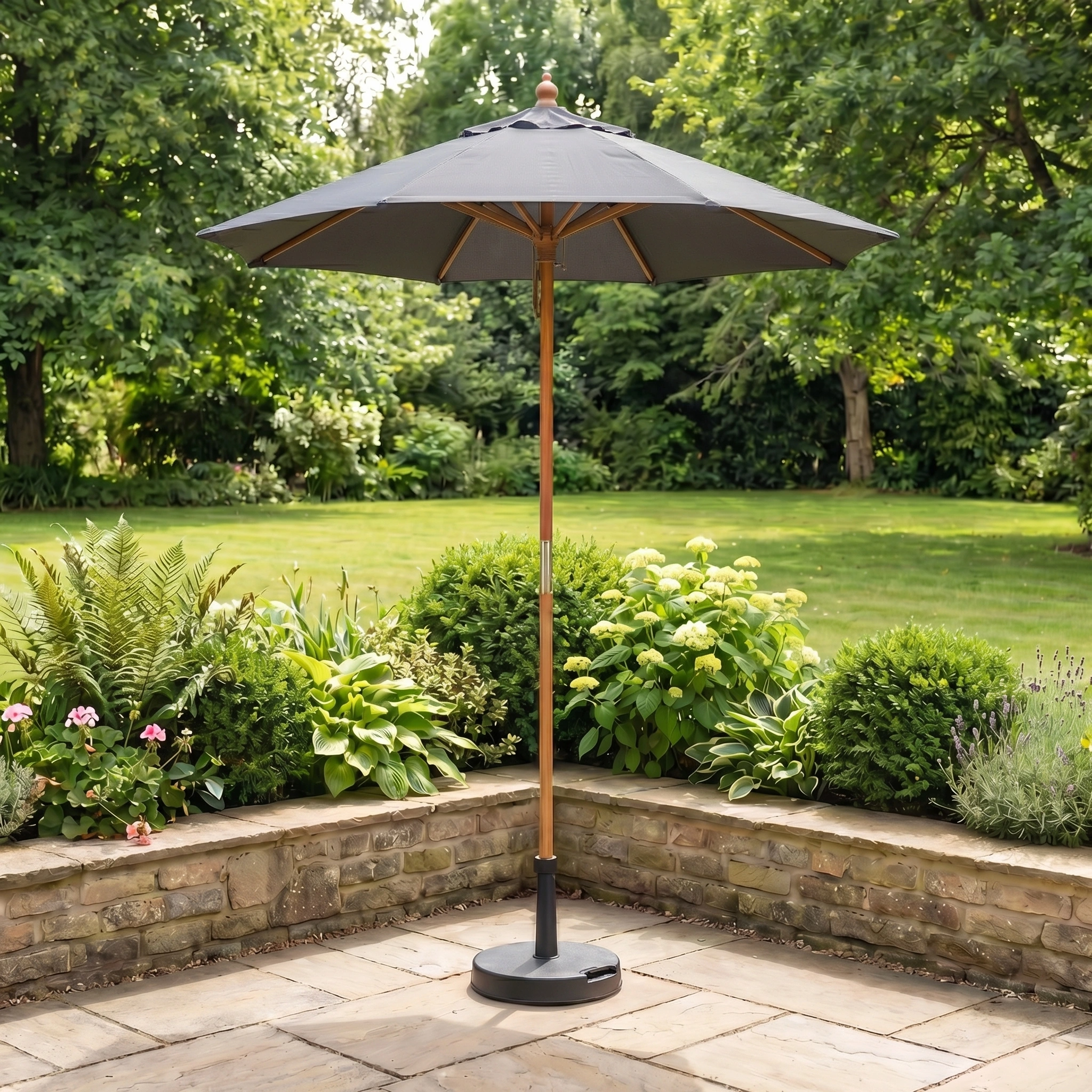 The Kratos 2m Round Wooden Parasol in Grey stands on a stone terrace, providing UV 50+ sun protection amid a lush green garden and trees.