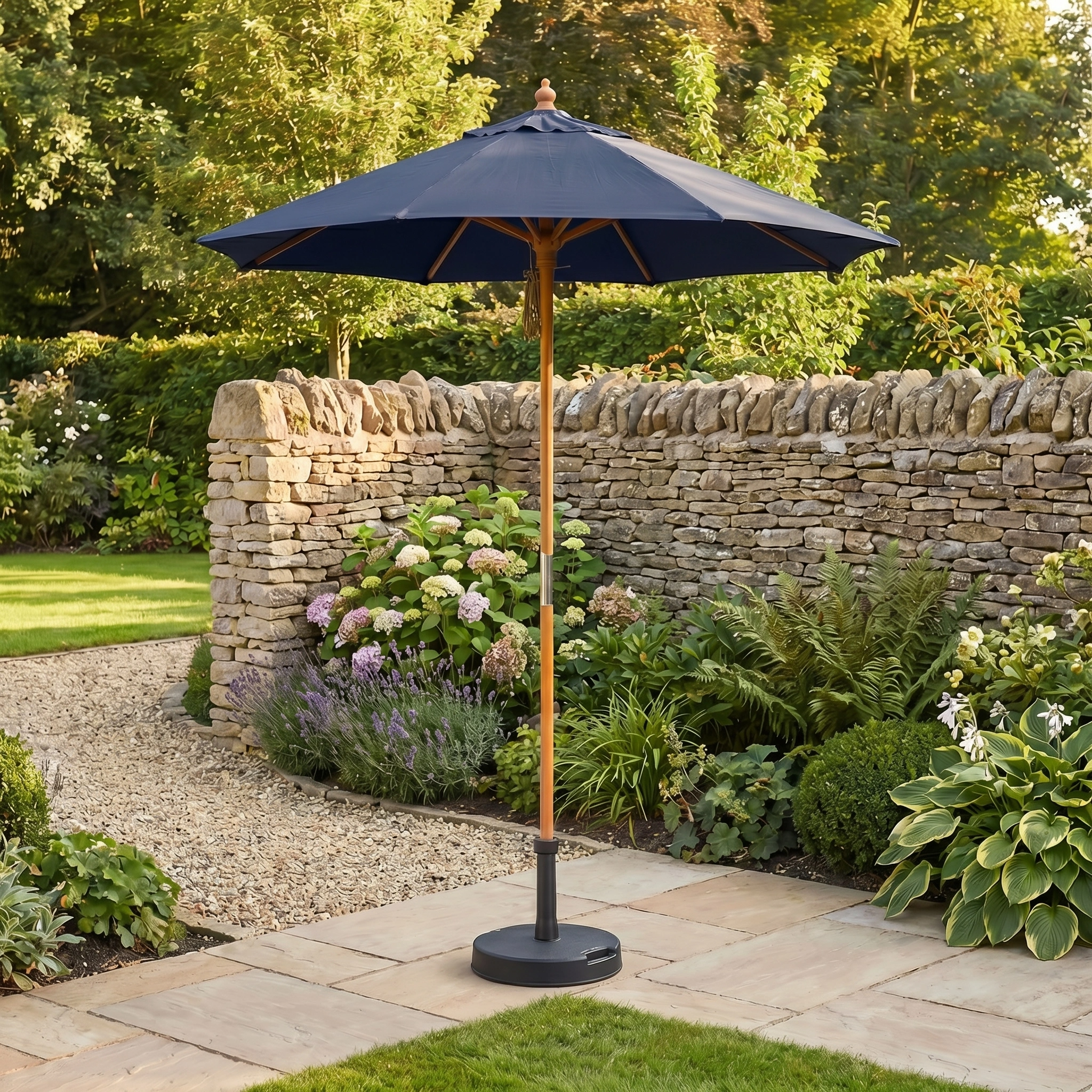 The Kratos 2m Round Wooden Parasol in Navy stands on a stone patio in a lush garden, bordered by a stone wall and vibrant plants.
