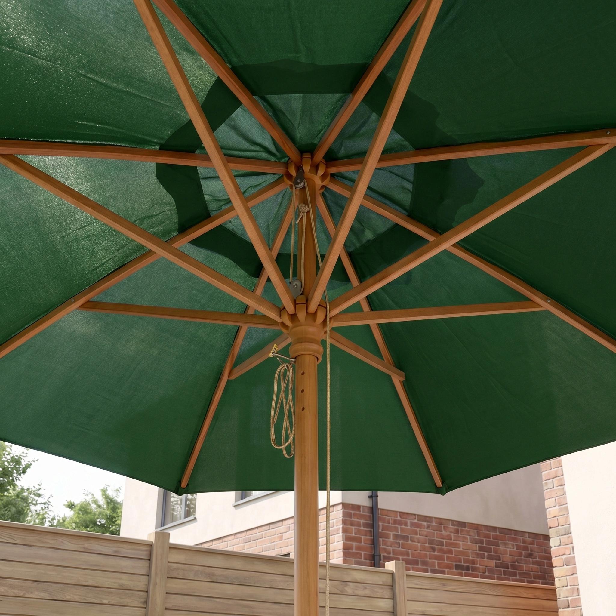 The Kratos 2m Round Wooden Parasol in Green, seen from below with strong wooden ribs and rope, stands stylishly by a fence and house—offering UV protection for your patio.