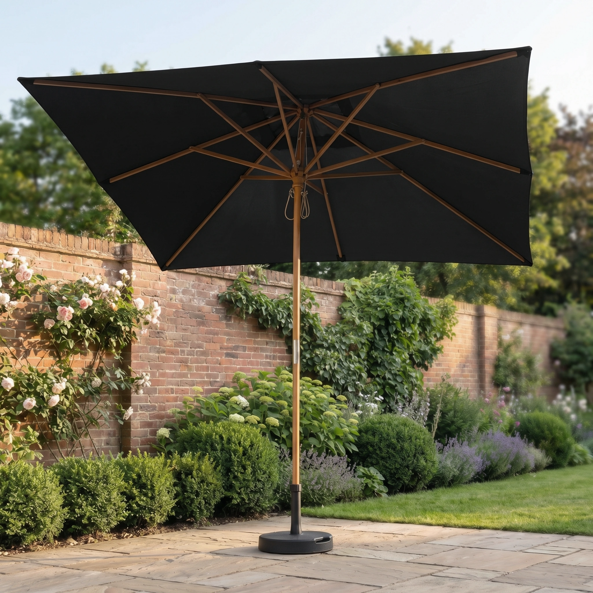 The Kratos 3m x 2m Rectangular Wooden Parasol in Black stands on a stone terrace in a landscaped garden, offering stylish sun protection with its UV 50+ rating.
