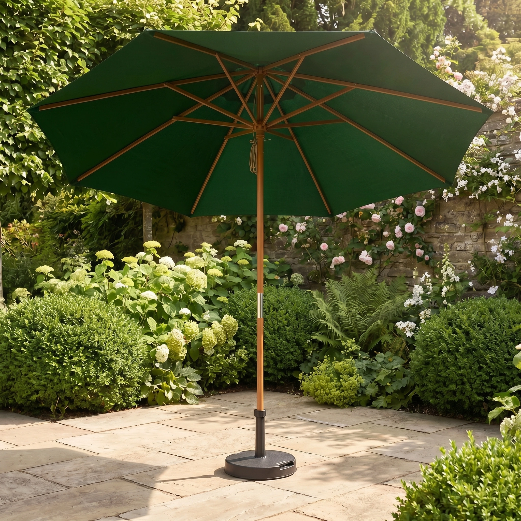 A Kratos 3m Round Wooden Parasol in Green stands on a stone patio among lush garden plants and flowers, providing stylish shade and UV protection.