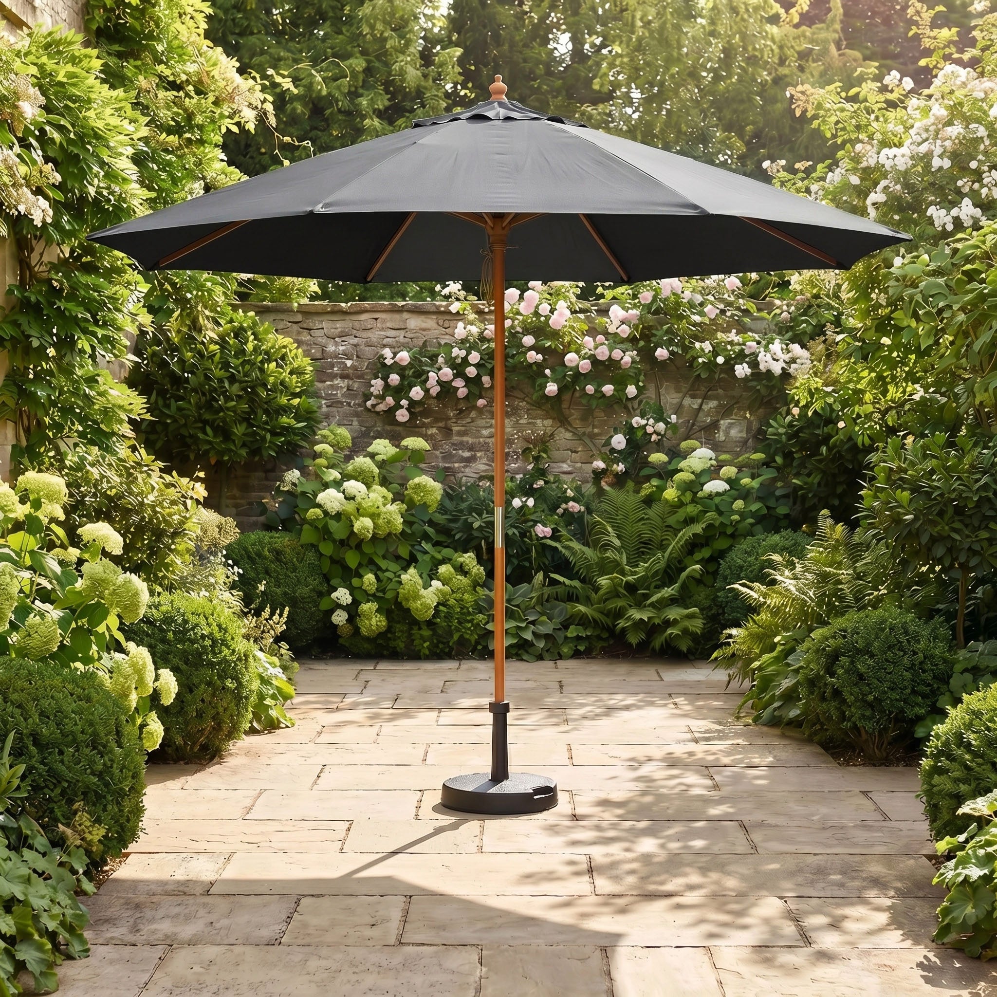 The Kratos 3m Round Wooden Parasol in Grey stands open in a sunlit garden, providing UV protection among lush green plants and vibrant flowers.