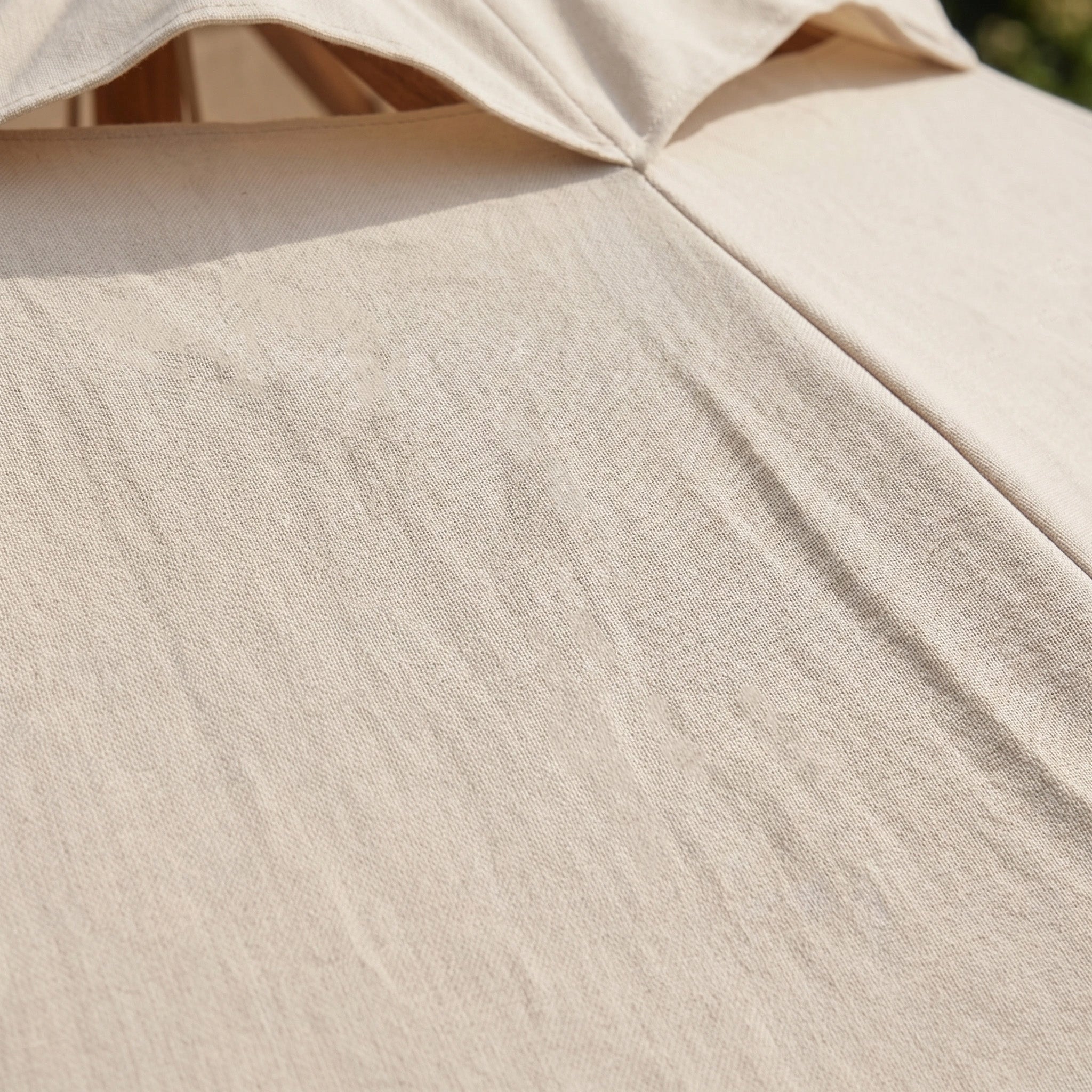 Close-up of the Kratos 3m Round Wooden Parasol in Beige, its textured canopy highlighted by sunlight. This outdoor umbrella offers UV 50+ protection, making it ideal for staying safe on sunny days.