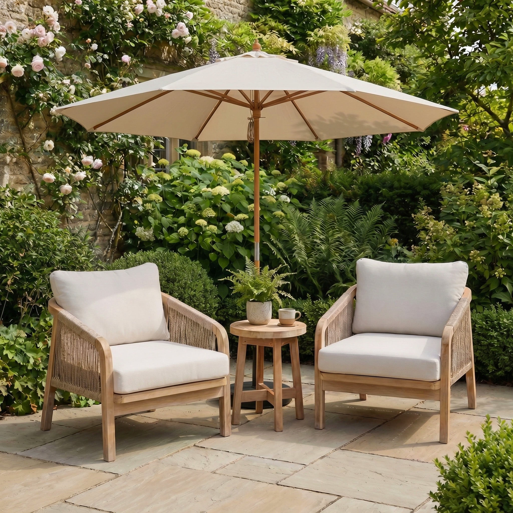 Two cushioned chairs and a small table sit under the Kratos 3m Round Wooden Parasol in Beige, providing UV protection in a lush garden setting.