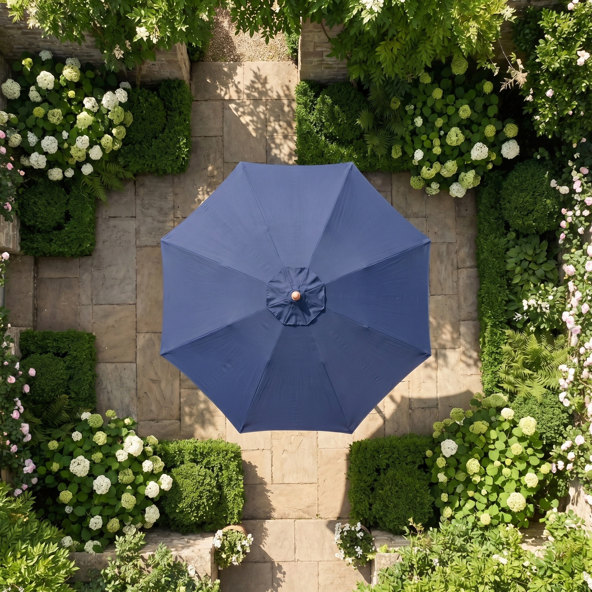The Kratos 3m Round Wooden Parasol in Navy stands at the center of a stone patio, surrounded by lush green plants and white flowers, providing UV 50+ sun protection.