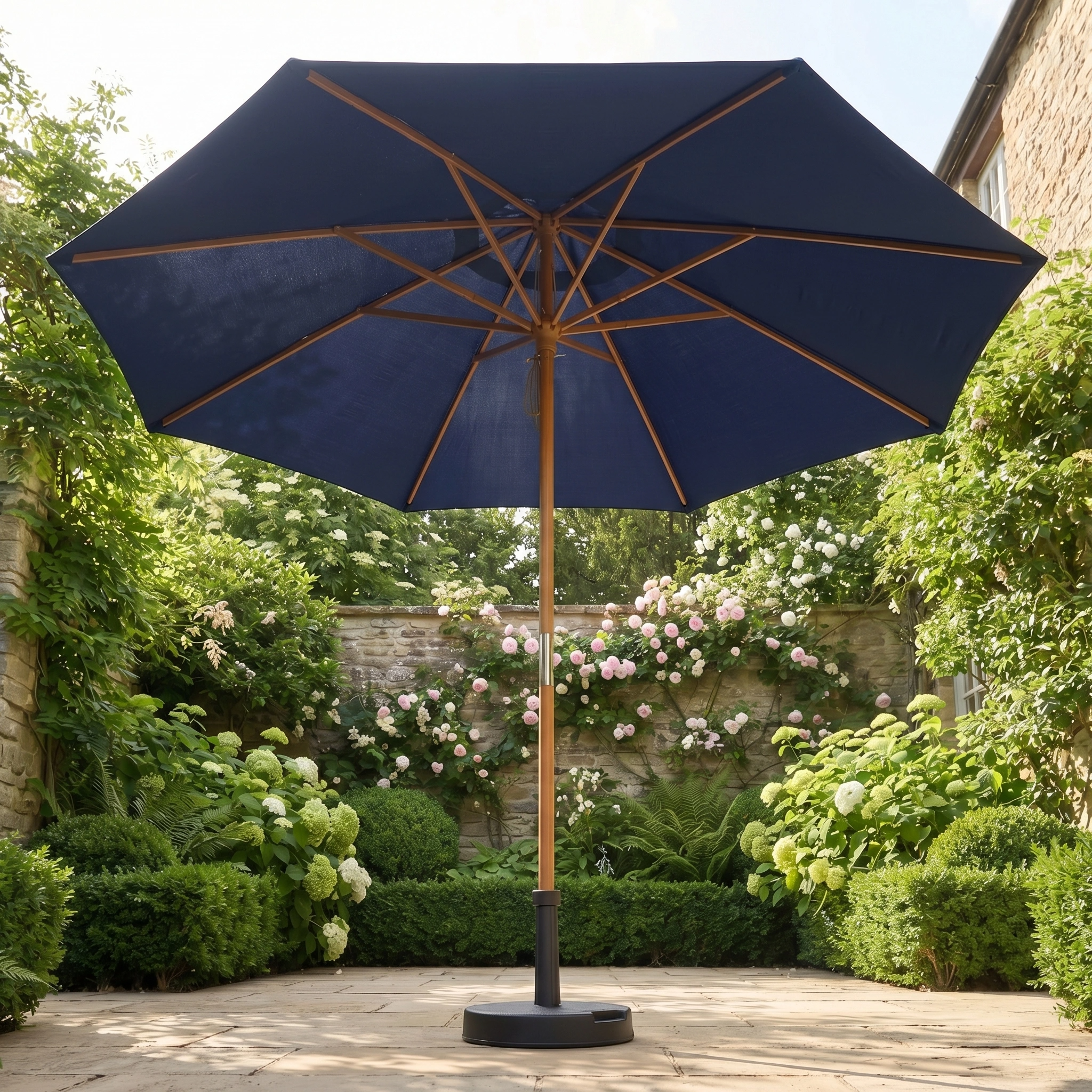 The Kratos 3m Round Wooden Parasol in Navy stands open in a sunny garden, its UV 50+ canopy providing shade among blooming flowers and green shrubs.