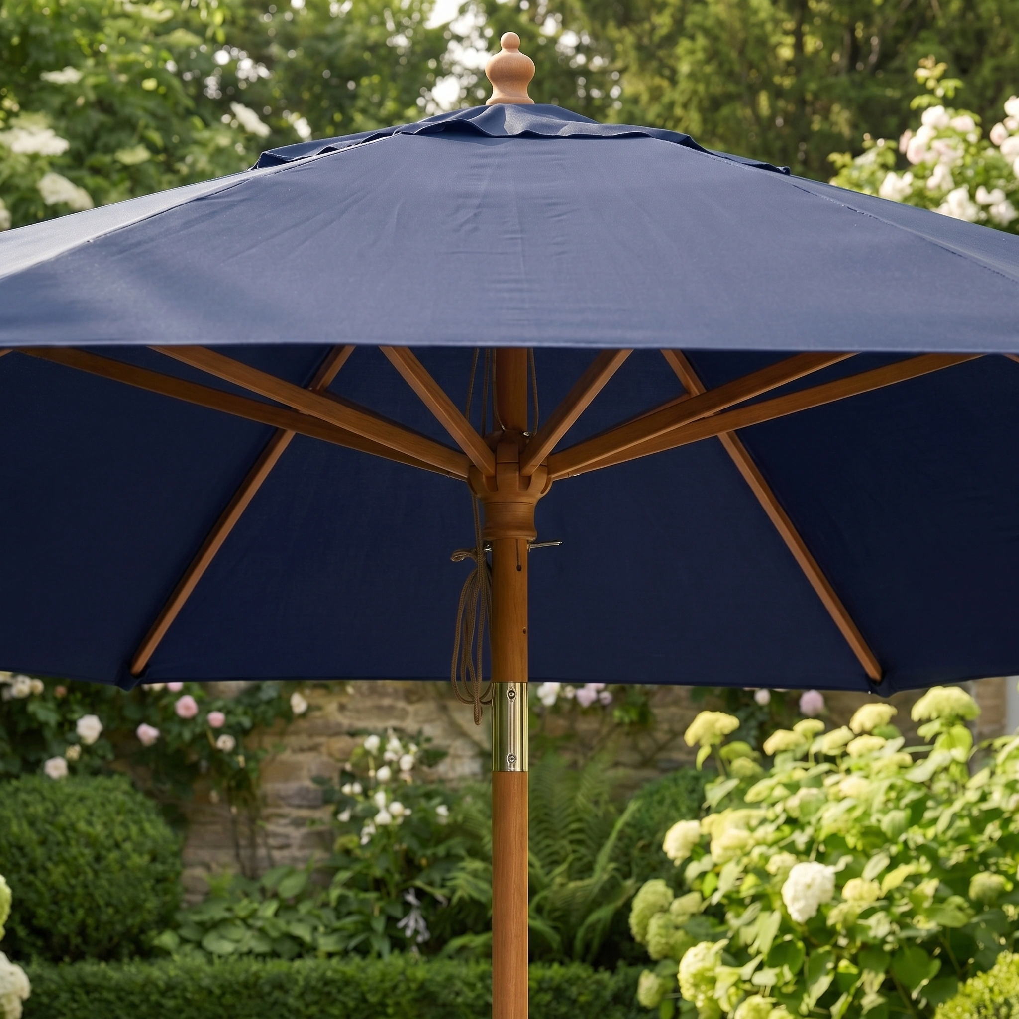 The Kratos 3m Round Wooden Parasol in Navy stands open in a lush green garden with blooming flowers, providing UV 50+ sun protection.