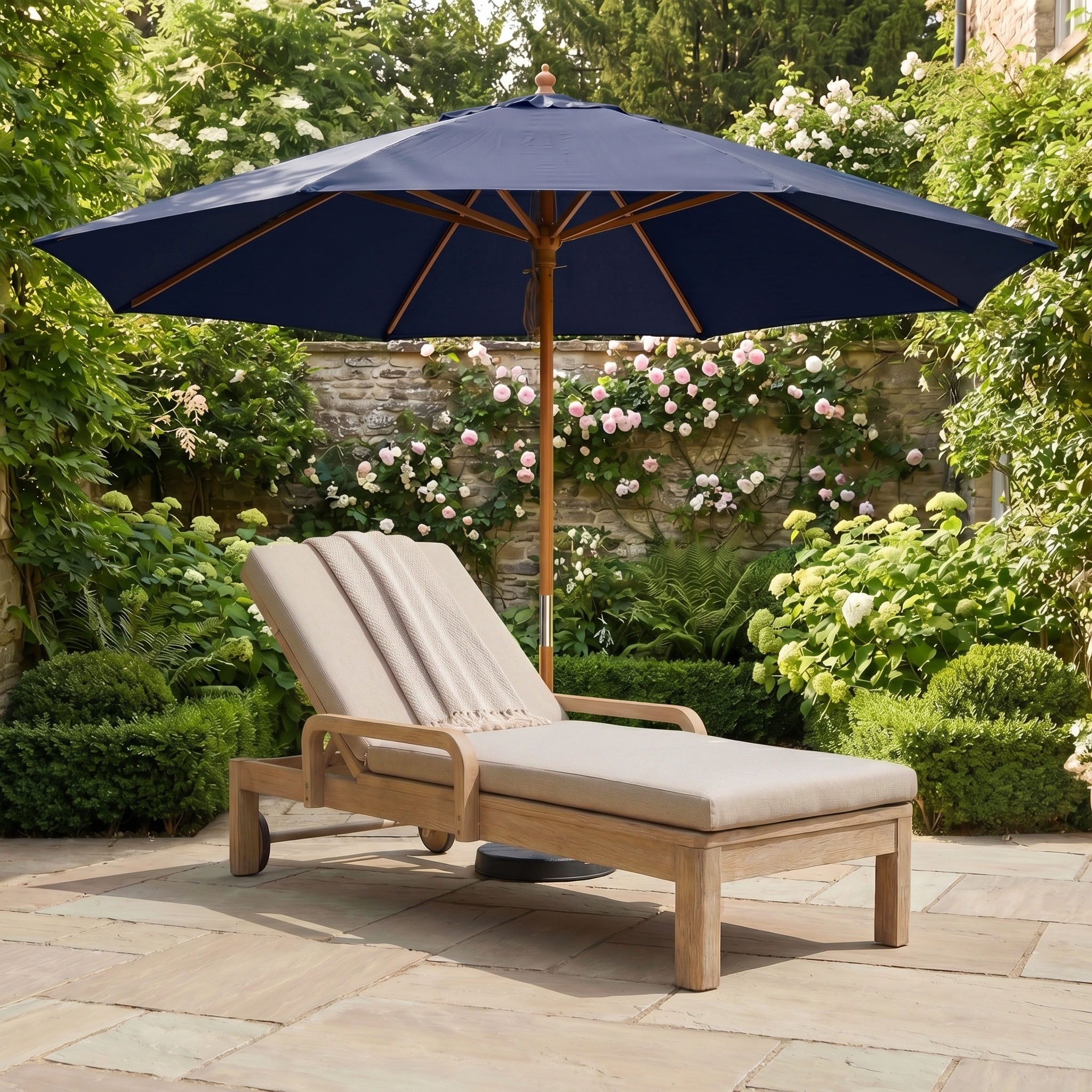 The Kratos 3m Round Wooden Parasol in Navy provides stylish shade and reliable UV protection over a wooden lounge chair with beige cushions and a towel on a garden patio.