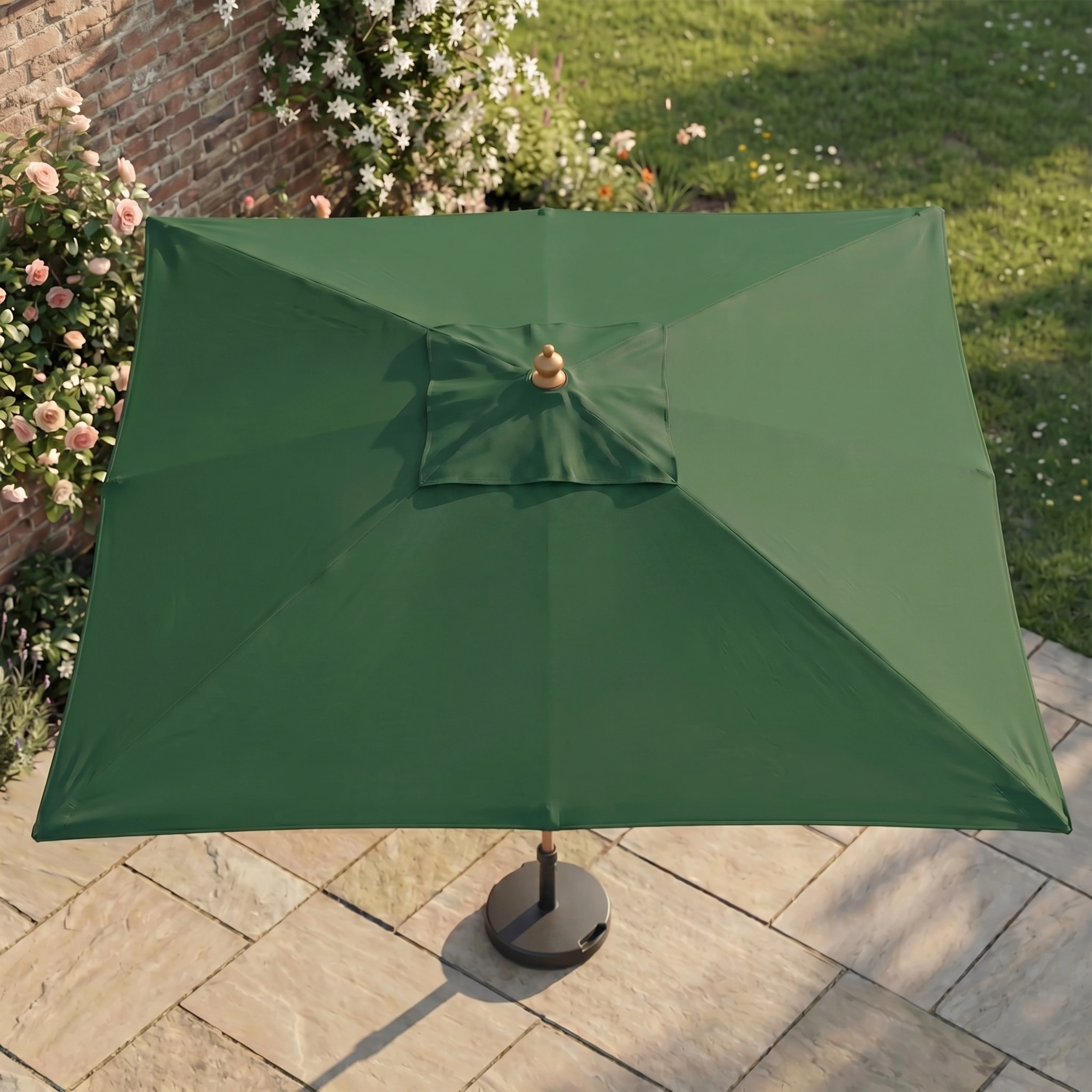 The Kratos 3m x 2m Rectangular Wooden Parasol in Green with UV protection stands on a stone patio, surrounded by blooming flowers and lush grass in the background.