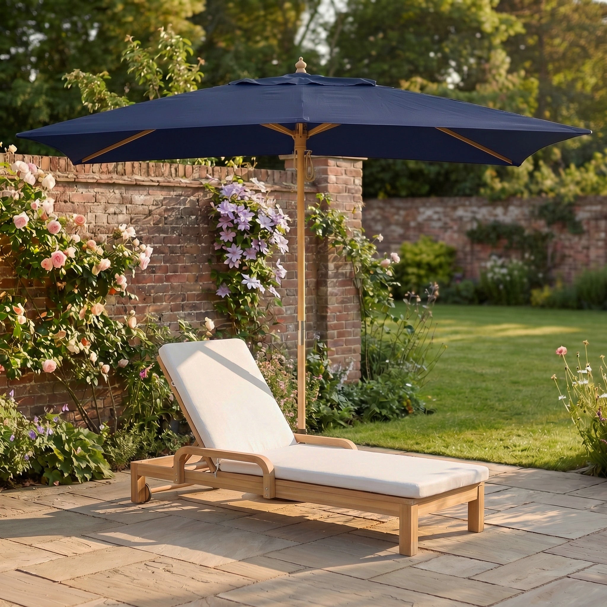 Wooden sun lounger with beige cushion under the Kratos 3m x 2m Rectangular Wooden Parasol in Navy (UV 50+) in a sunny, flower-filled garden bordered by a brick wall.