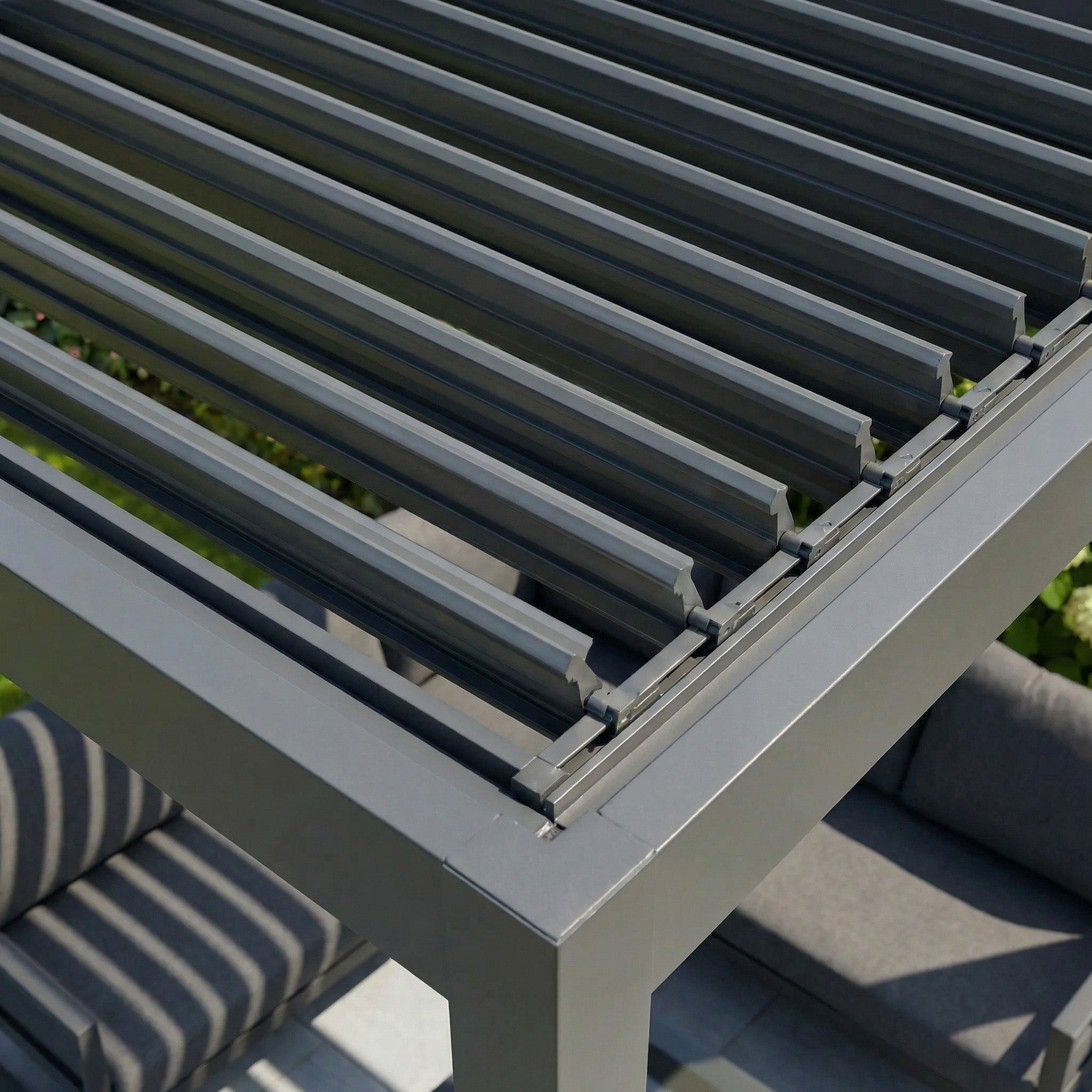 Close-up of the PergoSTET Lite Neo 3m x 7m Metal Rectangular Pergola in Grey, featuring manually tilting steel louvres for outdoor weather protection over a stylish seating area with cushions.