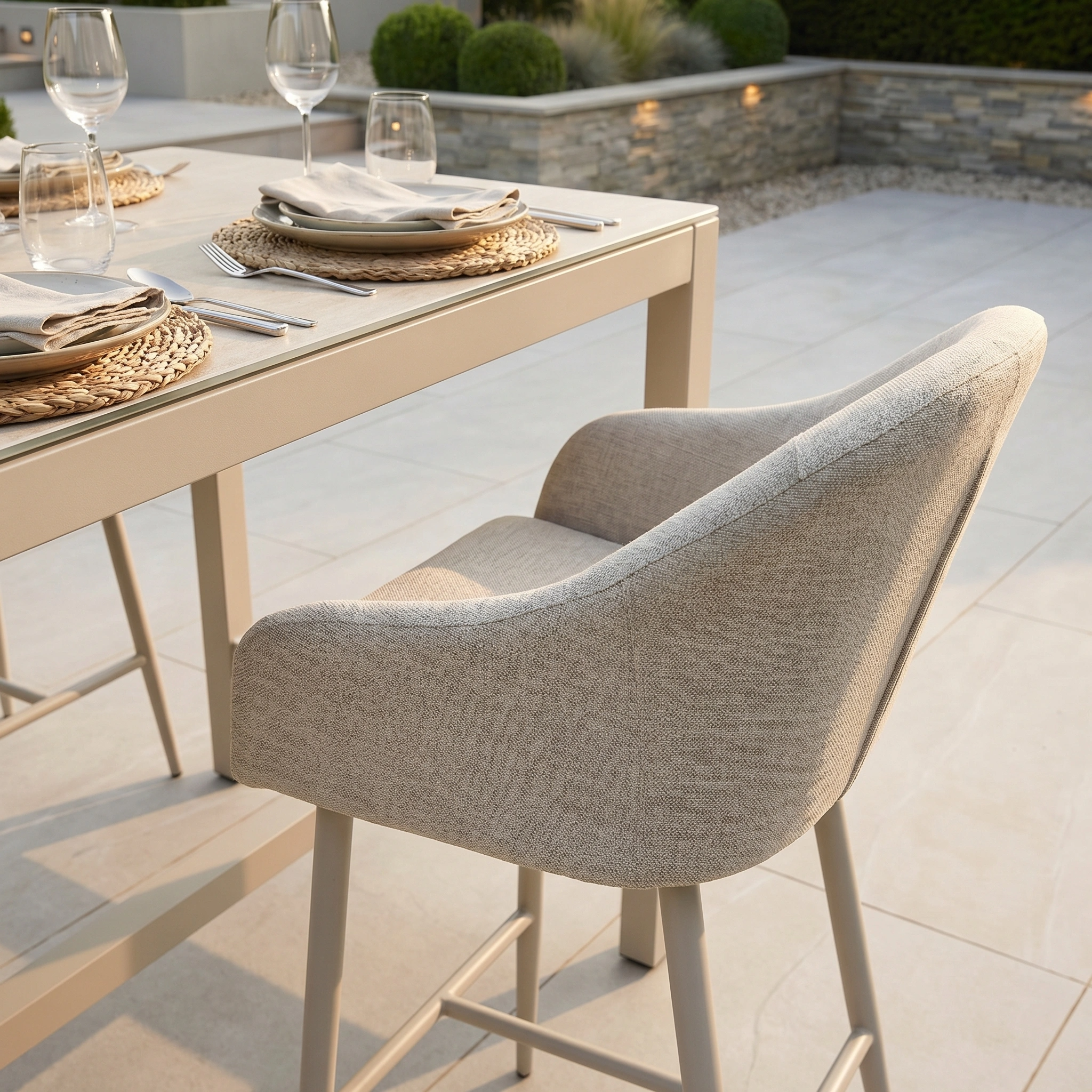 The Luna 8 Seat Bar Set in Fawn features cushioned beige chairs and durable outdoor fabric, complete with plates and glasses on a tiled patio for long-lasting comfort.