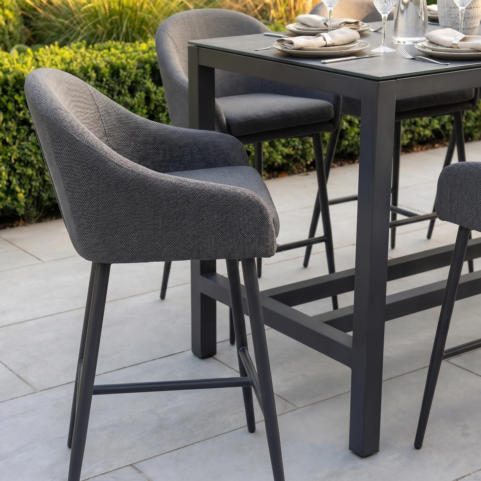 The Luna 8 Seat Bar Set in Grey features elegant, weather-resistant upholstery, perfect for outdoor patios surrounded by lush greenery.