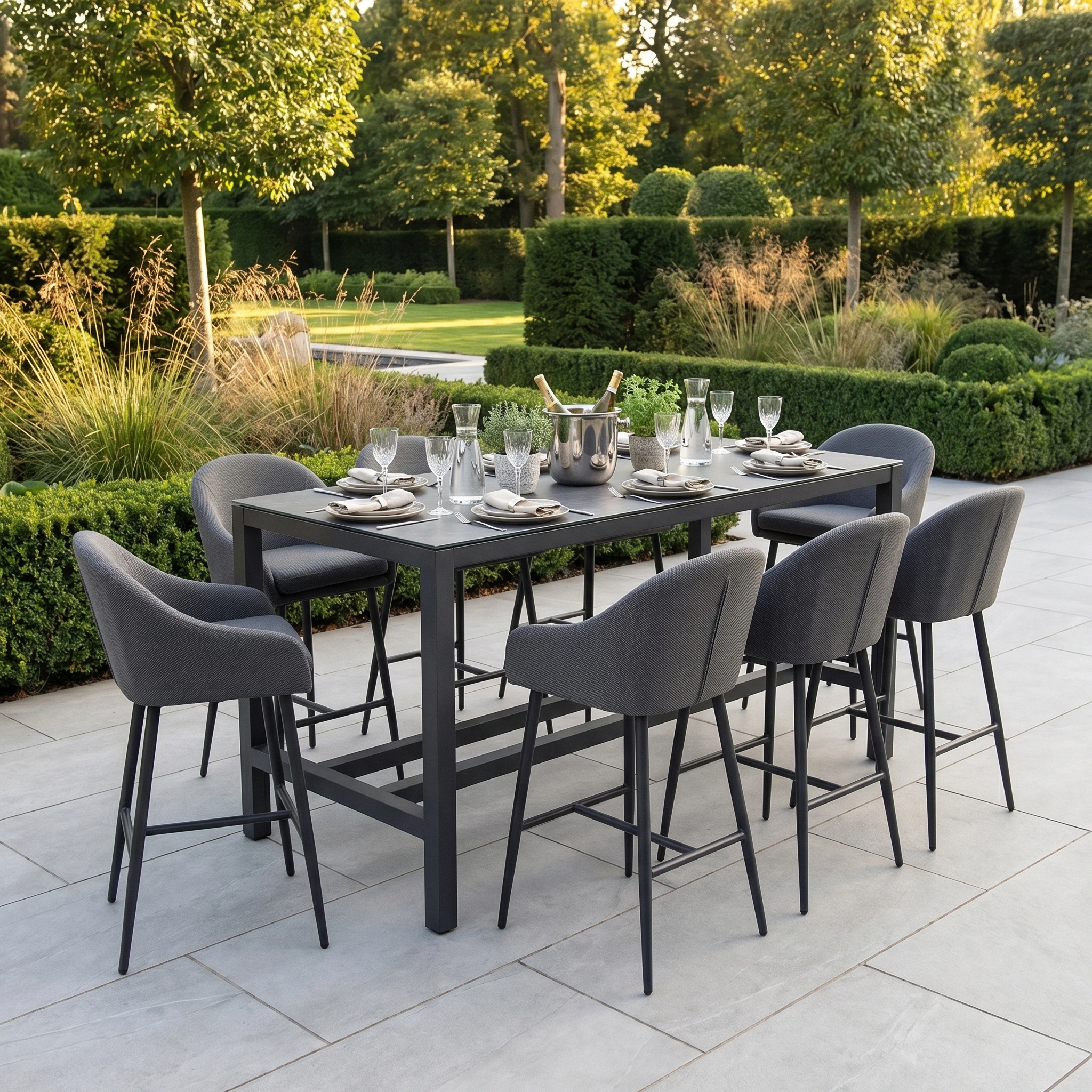 The Luna 8 Seat Bar Set in Grey, made from stain-resistant materials, stands elegantly in a manicured garden surrounded by trees and hedges.