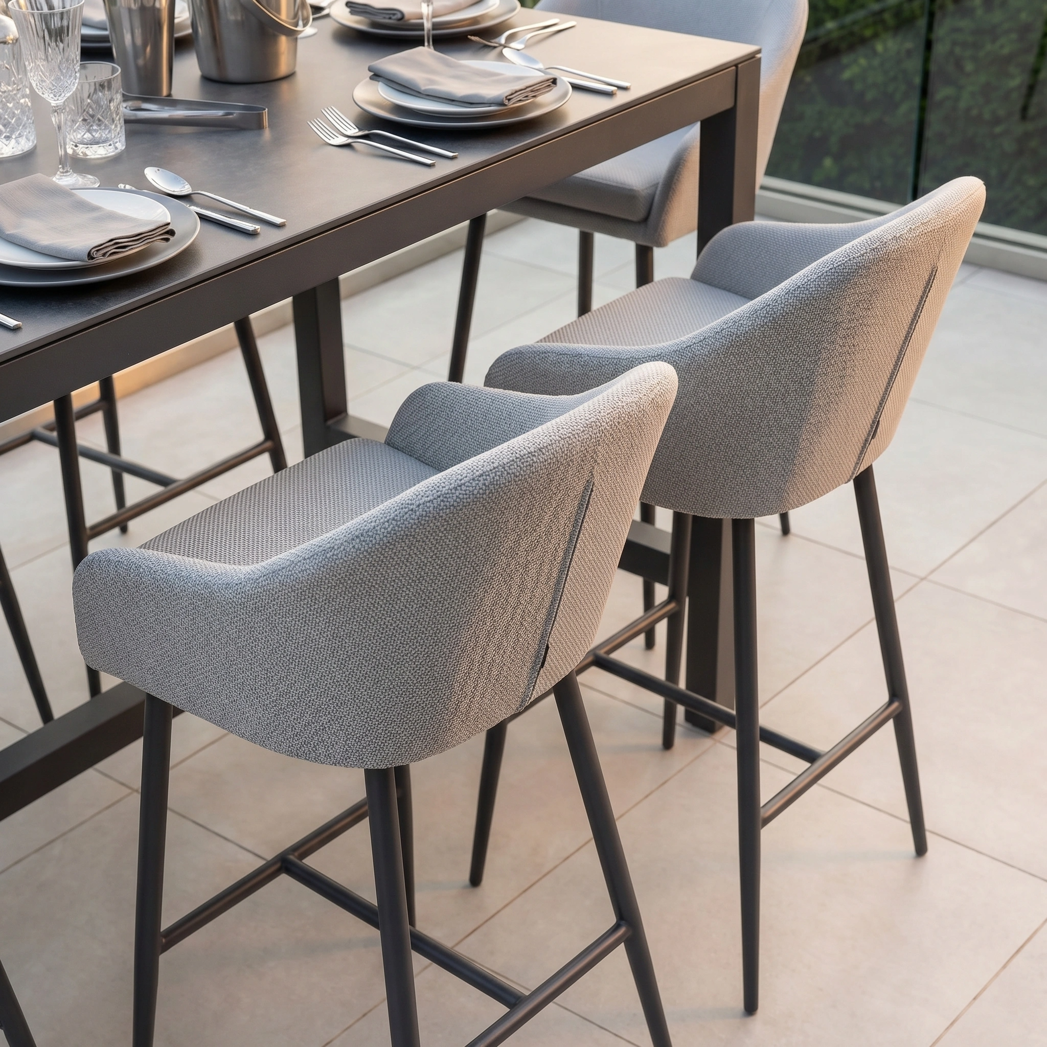 The Luna 8 Seat Bar Set in Oyster Grey features modern cushioned barstools with durable outdoor fabric, arranged at a dining table on tiled flooring—blending style and comfort for any all-weather setting.