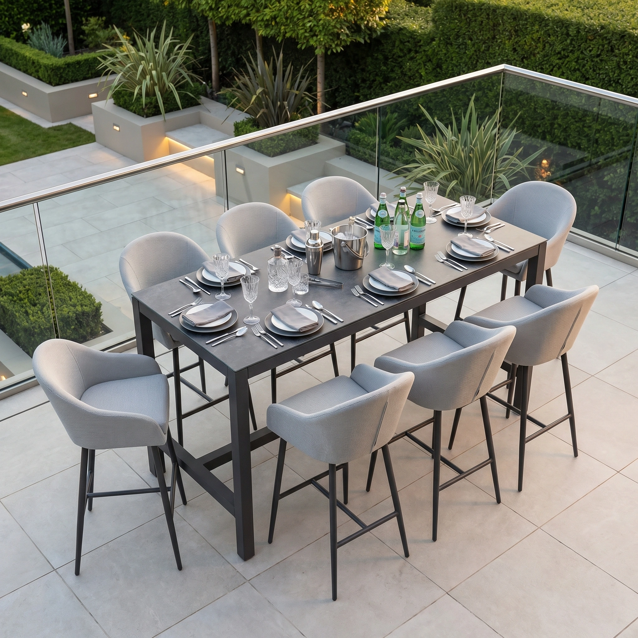 The Luna 8 Seat Bar Set in Oyster Grey features eight outdoor chairs with matching fabric, arranged on a patio with glassware, plates, and bottled drinks for a modern dining experience.