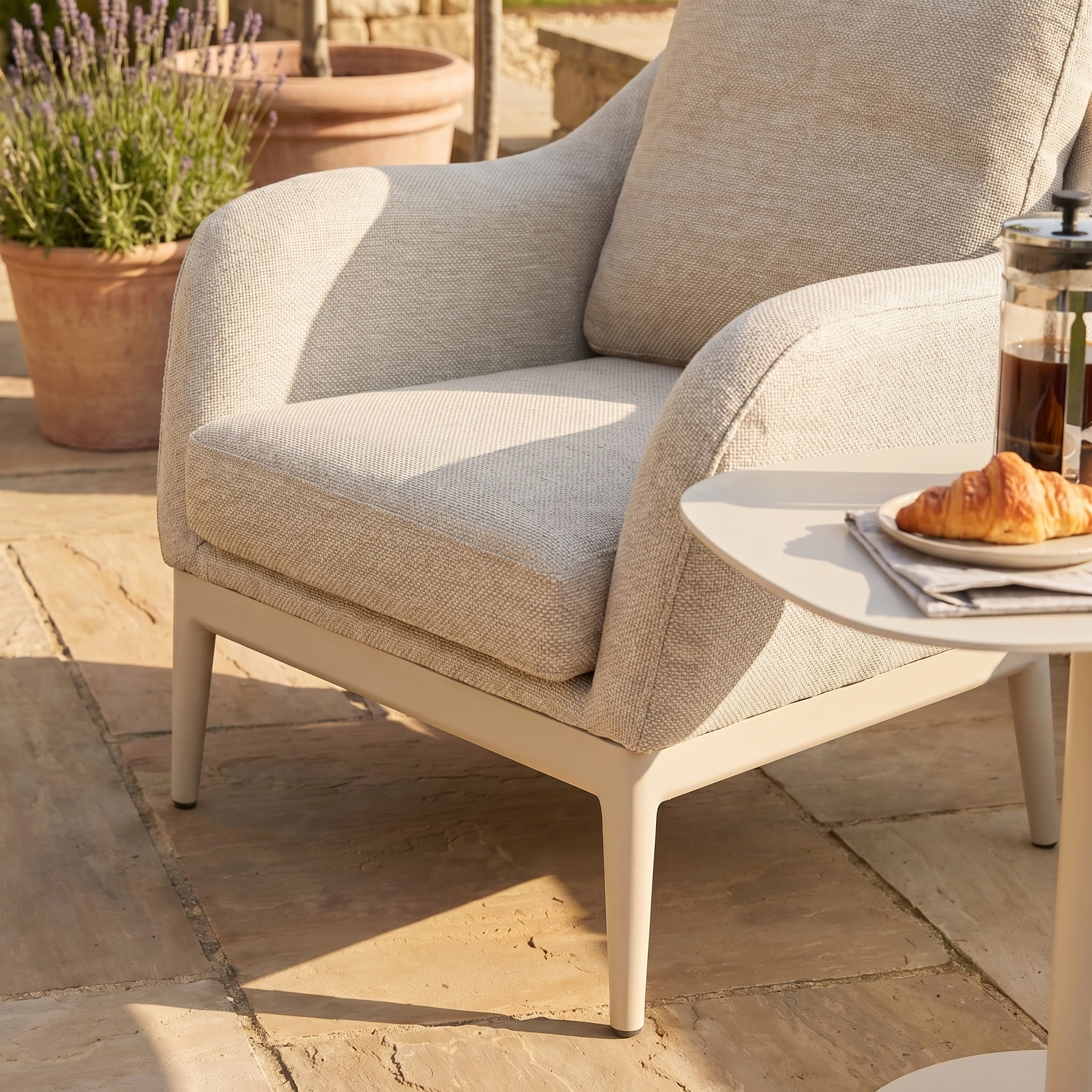 Luna Armchair in Fawn set beside a table with a croissant and coffee on a sunny, stain-proof stone patio.