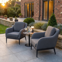 Two Luna Armchairs in Grey with outdoor fabric and a small table holding drinks sit on a modern patio garden at sunset.