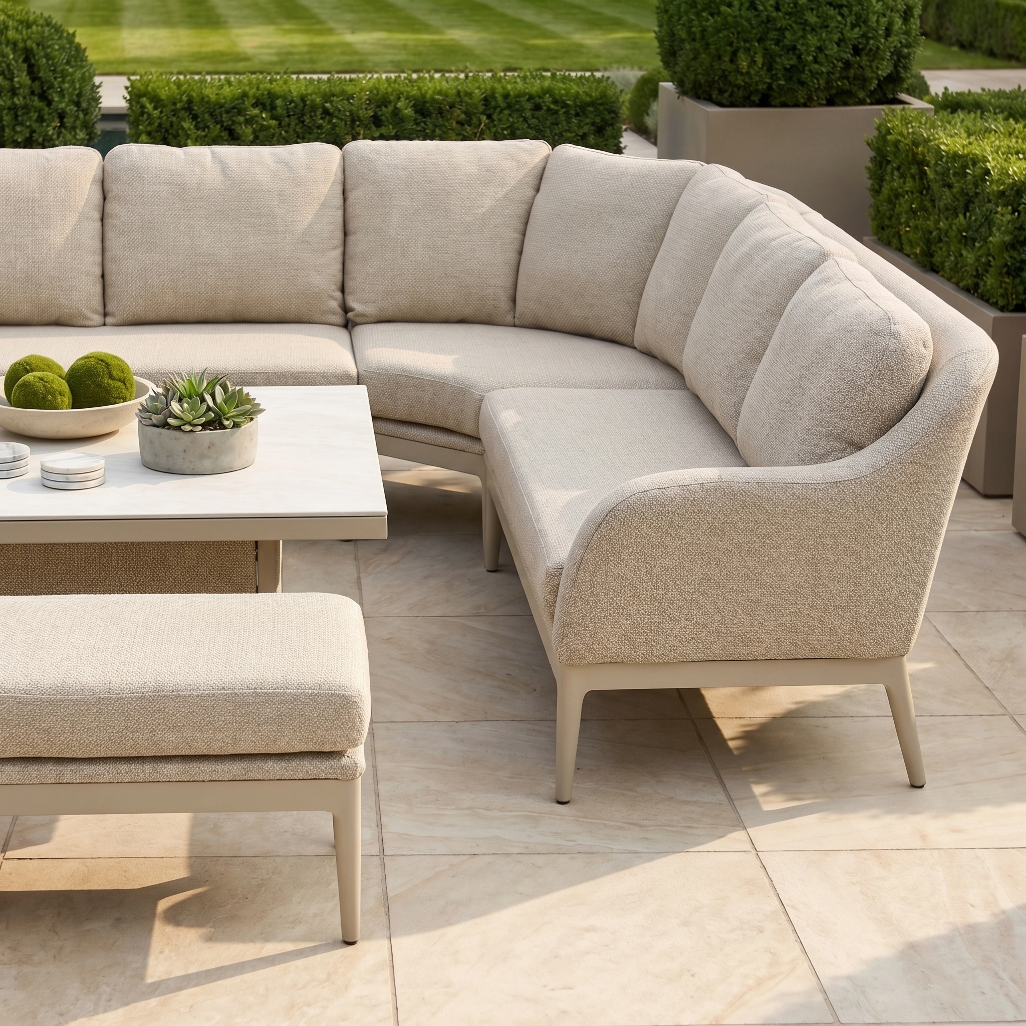 Luna Deluxe Outdoor Fabric Square Corner Dining Set with Rising Table in Fawn, shown with matching cushions and bench on a tiled patio, green lawn in the background.