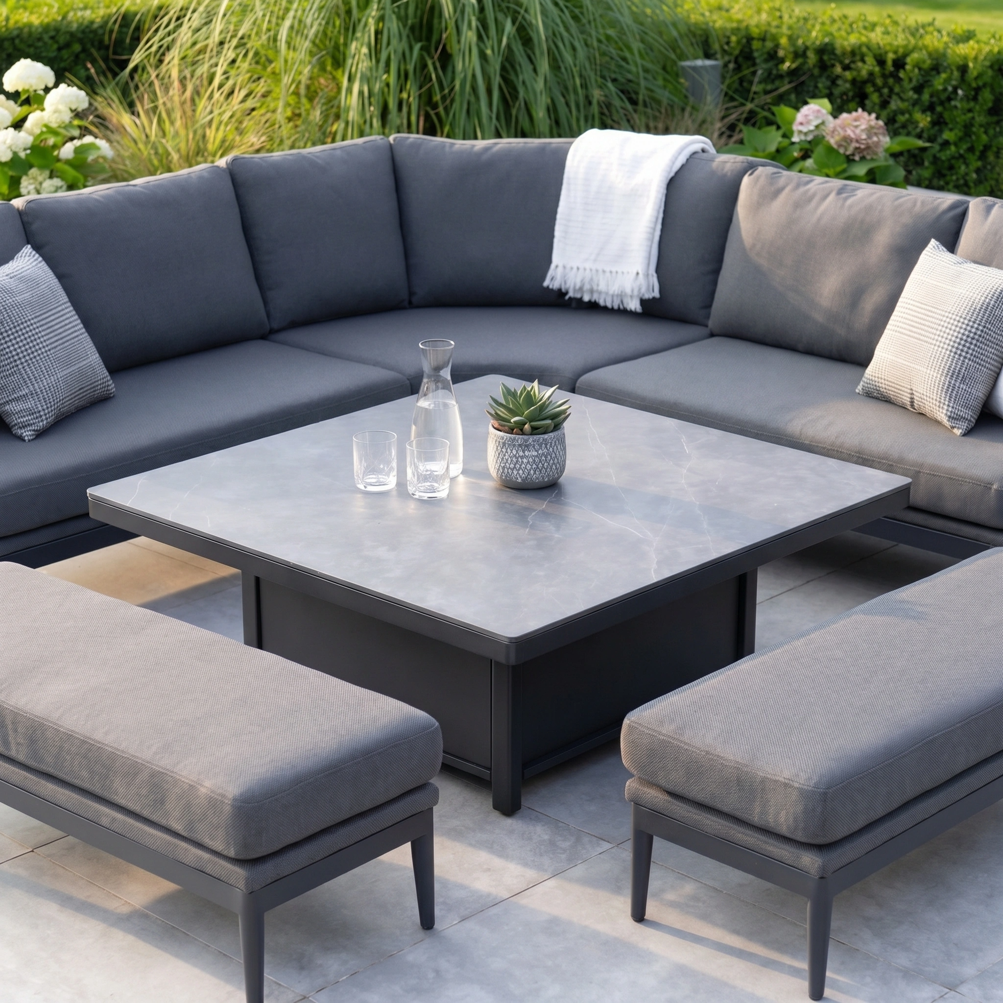 Modern patio featuring the Luna Deluxe Outdoor Fabric Square Corner Dining Set with Rising Table in Grey. All-weather materials ensure year-round durability and comfort for stylish outdoor dining and lounging.