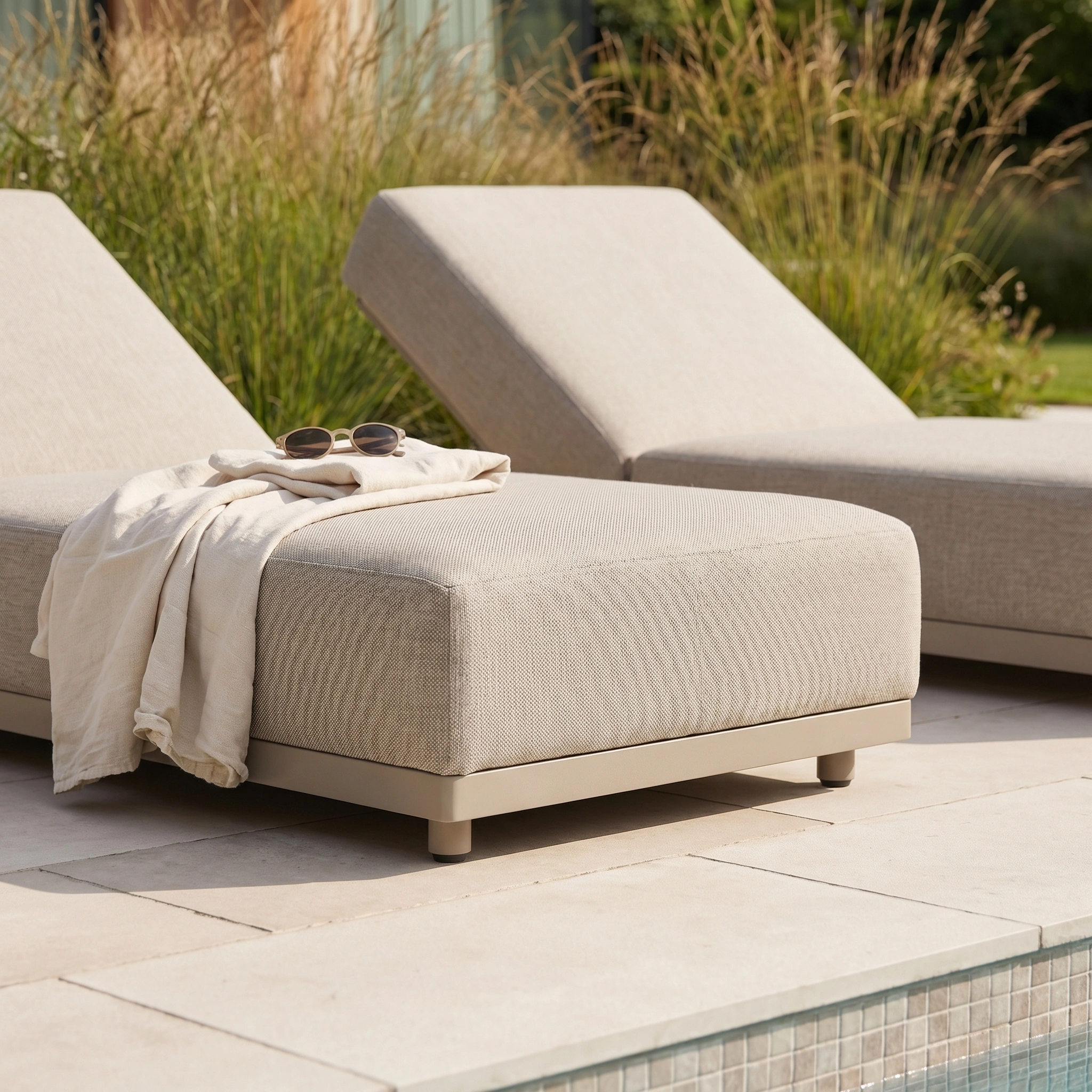 The Luna Outdoor Fabric Deluxe Sun Lounger in Fawn sits by the pool, topped with a light blanket and sunglasses—its stain-resistant fabric ensures effortless style and easy care for outdoor living.