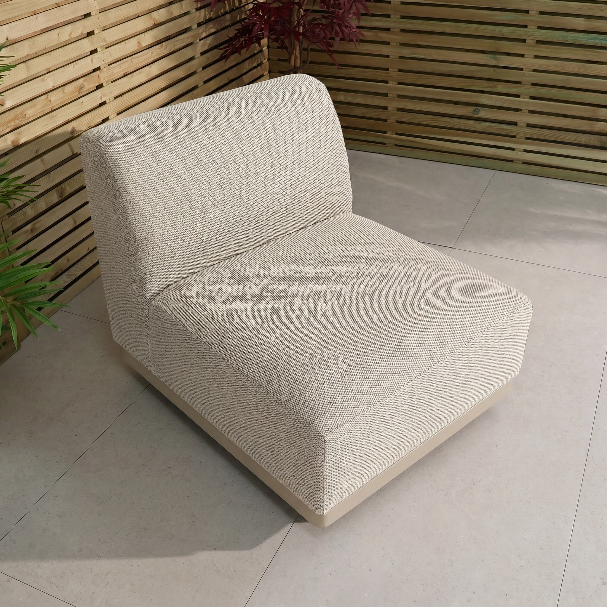 A Luna Outdoor Fabric Middle Extension Piece in Fawn sits on a tiled patio, framed by wooden slat fencing and greenery—a welcoming addition to any outdoor lounging area.