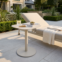 A lounge chair and the Luna Side Table in Latte (45cm x 45cm) with a drink, olives, and magazines on a sunlit patio—perfect for relaxing with maintenance-free outdoor furniture.