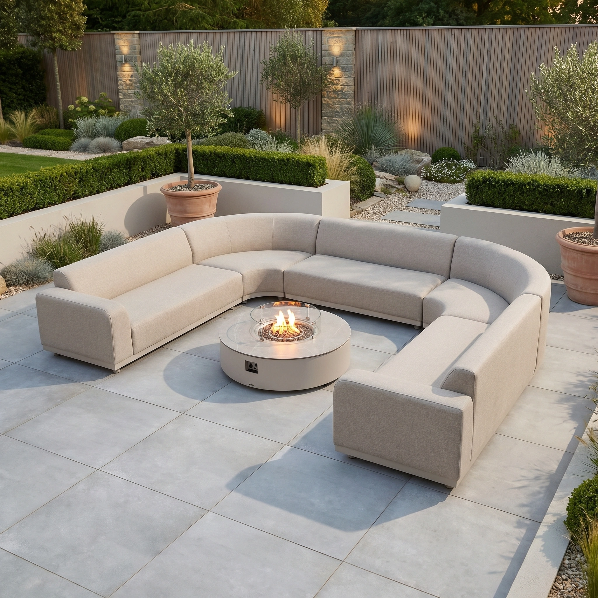 The Luna U-Shape Outdoor Fabric Curved Corner Group with Round Firepit Coffee Table in Fawn creates a cozy setting on a tiled patio in a modern landscaped garden.