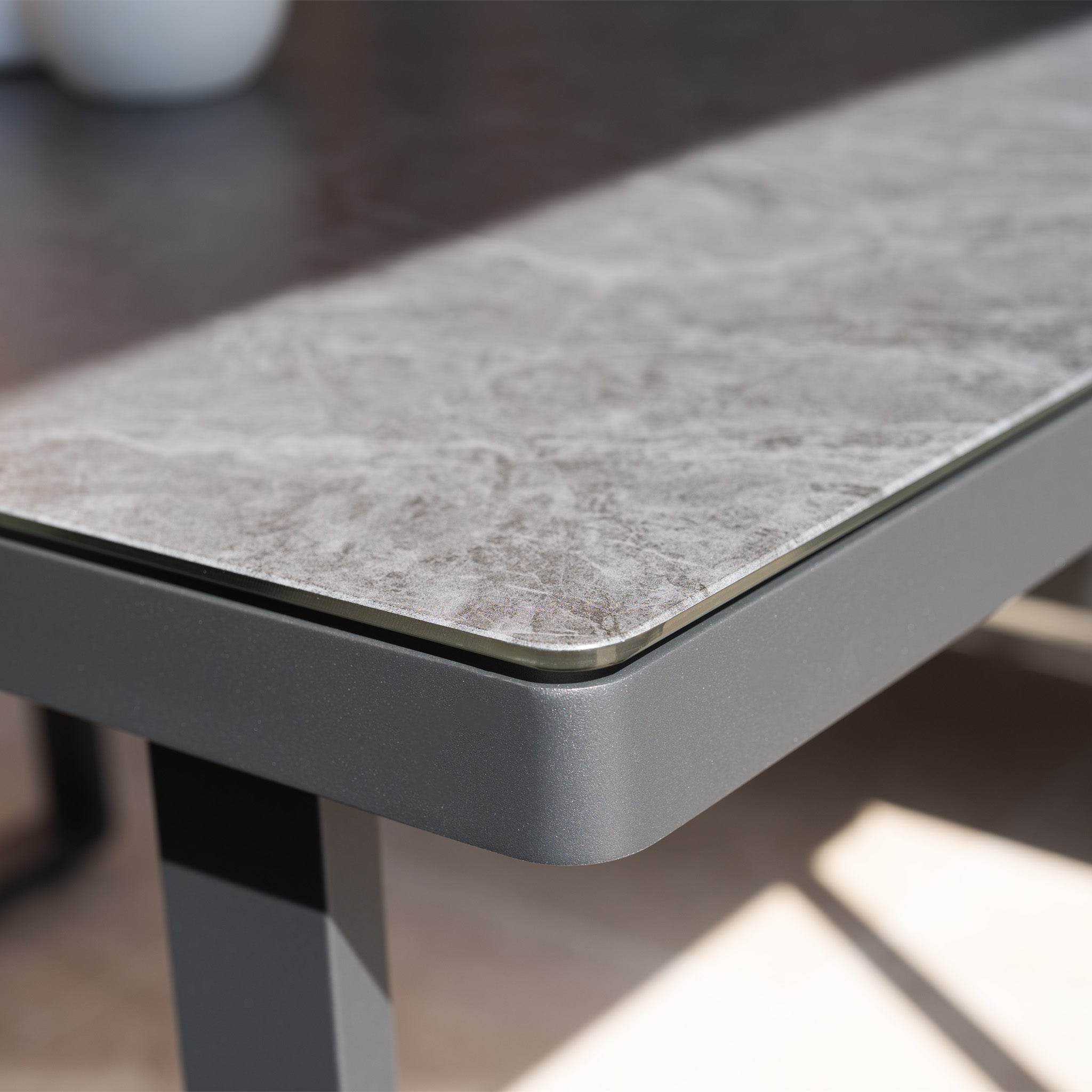 Close-up of the Lyra Corner Dining Set in Charcoal, featuring a gray stone-textured top and black aluminium frame legs—perfect for stylish outdoor gatherings in natural light.