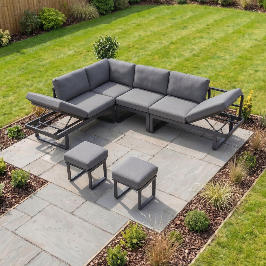 The Lyra Corner Dining Set in Charcoal features gray cushioned seats, a table for four, and stools—perfect for elevating your garden with modern style on a stone patio.