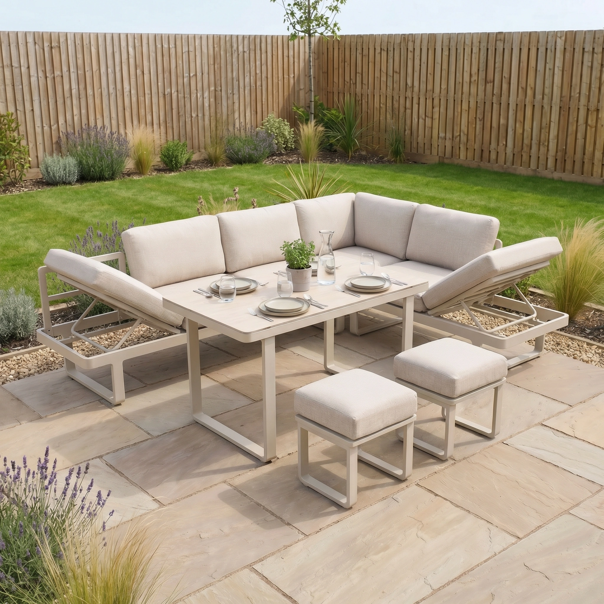 Lyra Corner Dining Set in Latte with aluminium sofa, table, and stools on a stone terrace in a fenced garden—ideal outdoor furniture for relaxing and entertaining.