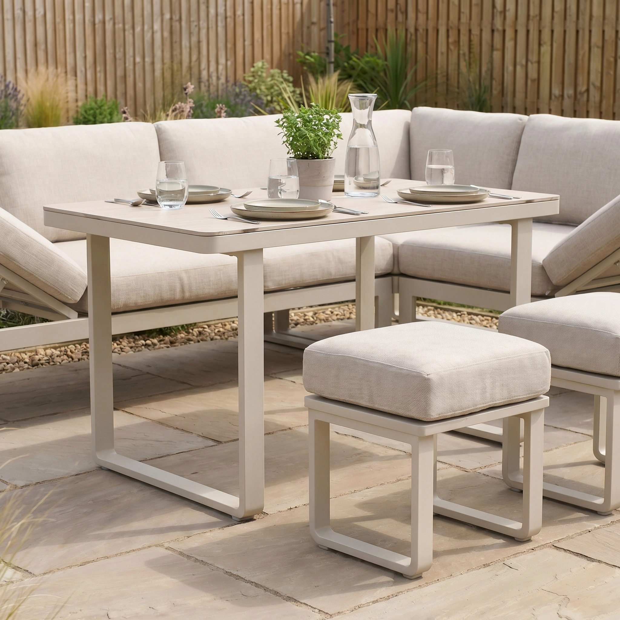 Modern outdoor patio set featuring the Lyra Corner Dining Set in Latte with beige cushions, sleek aluminium sofa, dining table for four, and a potted plant centerpiece.