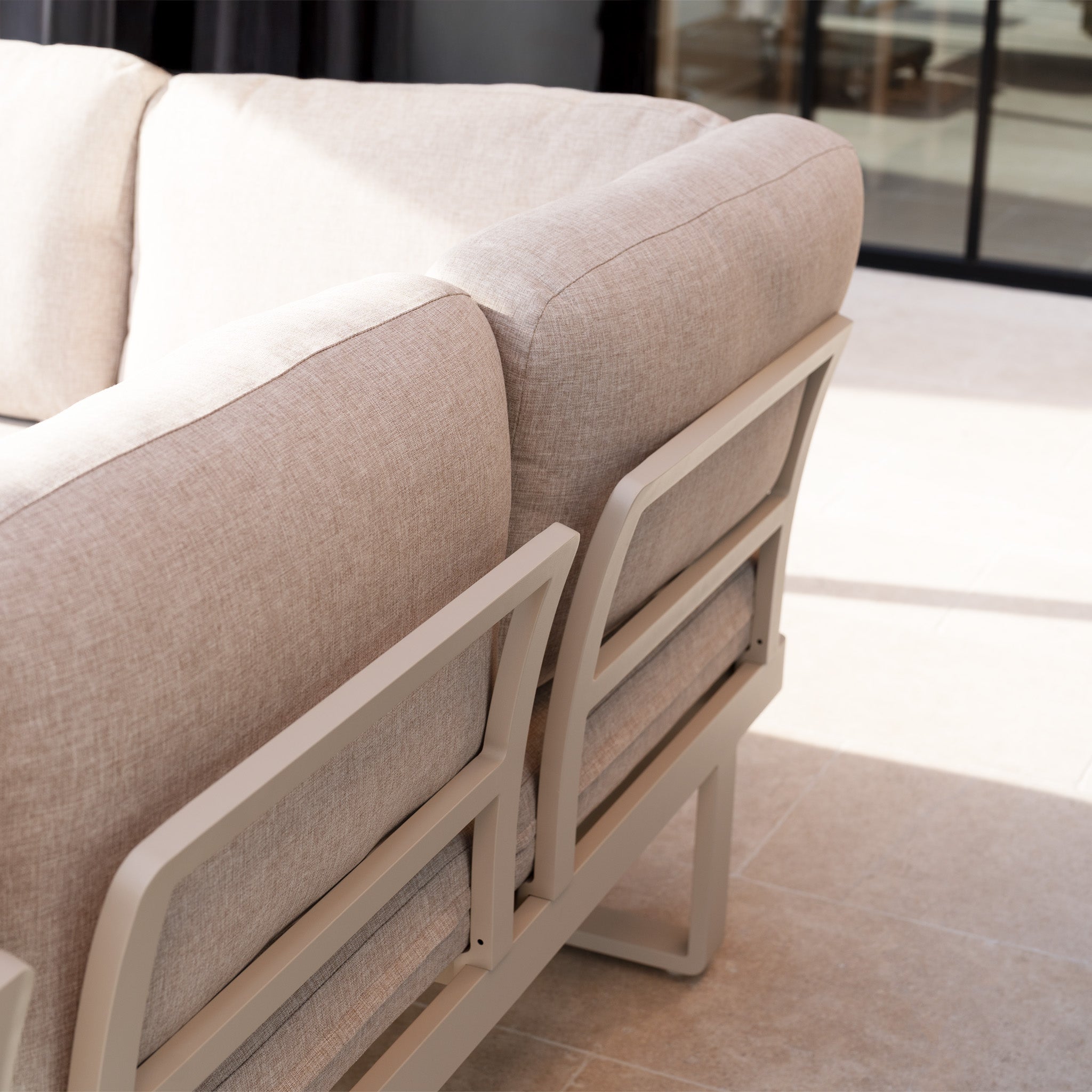 The Lyra Corner Dining Set in Latte features beige cushions and a sleek aluminium frame, making it an inviting outdoor furniture piece ideal for patios near glass doors.