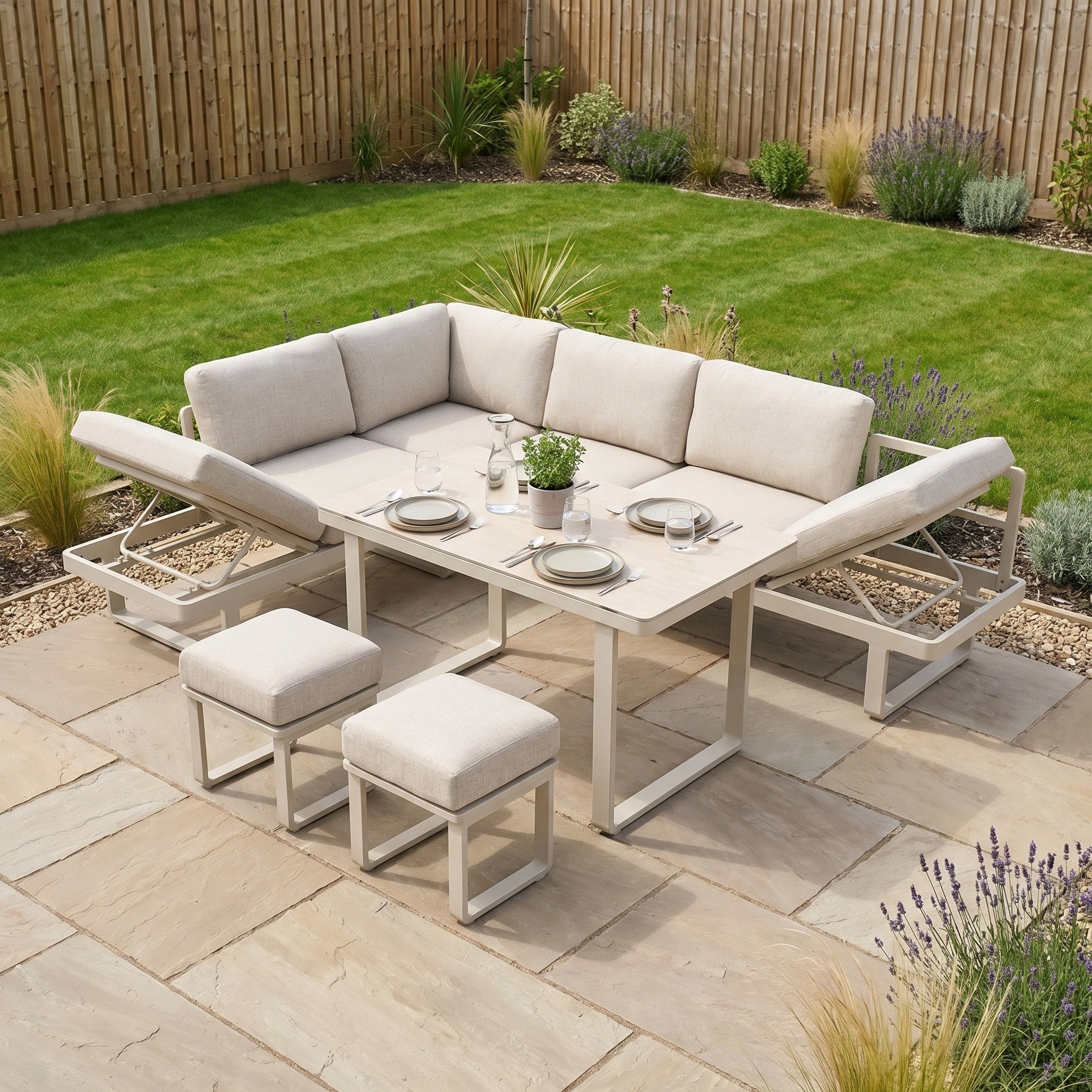 The Lyra Corner Dining Set in Latte, featuring cream cushions and an aluminium sofa, comfortably seats four on a stone patio in a landscaped garden.