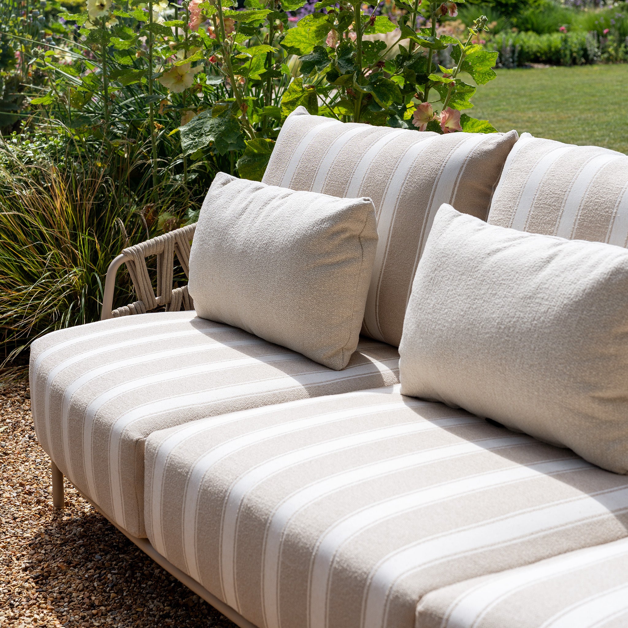 The Madeira 3 Seat Sofa in Striped Latte (Ex Display) showcases a beige and white striped design and comes with two inviting cushions, making it the perfect outdoor garden furniture for relaxing in a tranquil setting.