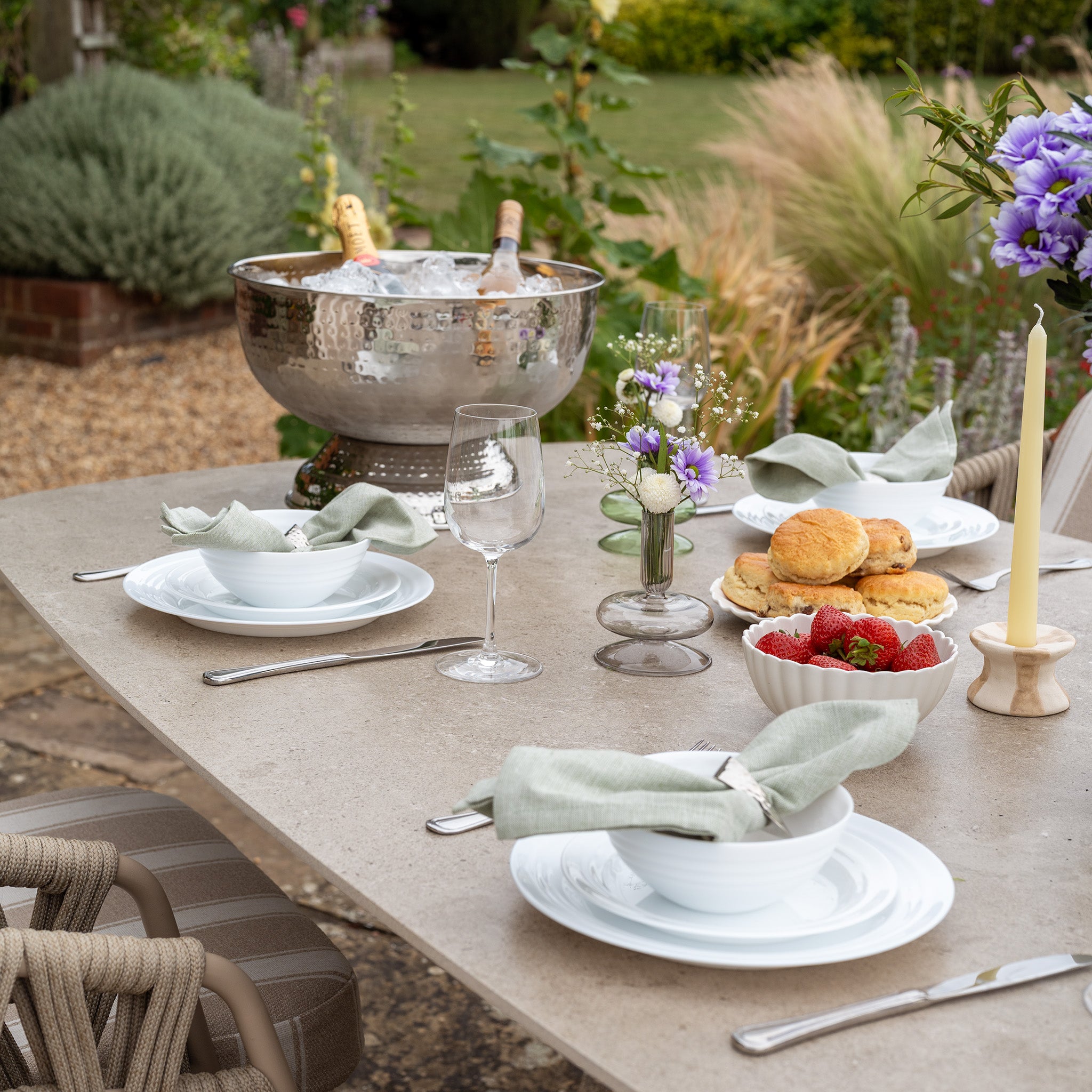 The Madeira 6 Seat Curved Rectangular Dining Set in Striped Latte features an aluminium table, perfect for elegant outdoor gatherings with plates, scones, strawberries, flowers, wine glasses, and a champagne bucket.