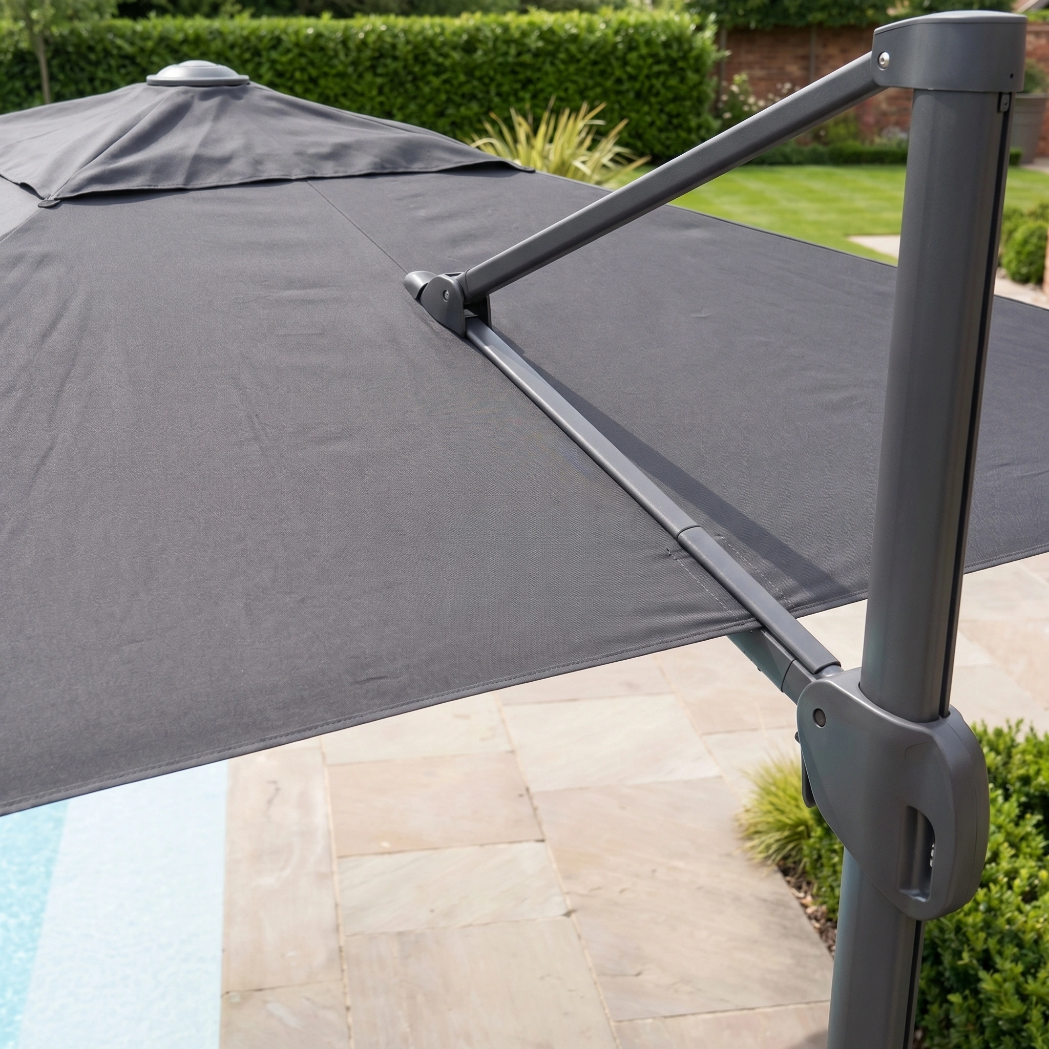 Close-up of the Nexus T2 Premium 3m Square Cantilever Parasol in Black with a 90kg granite base, featuring 360-degree rotation, by a stone patio next to a pool and green garden.