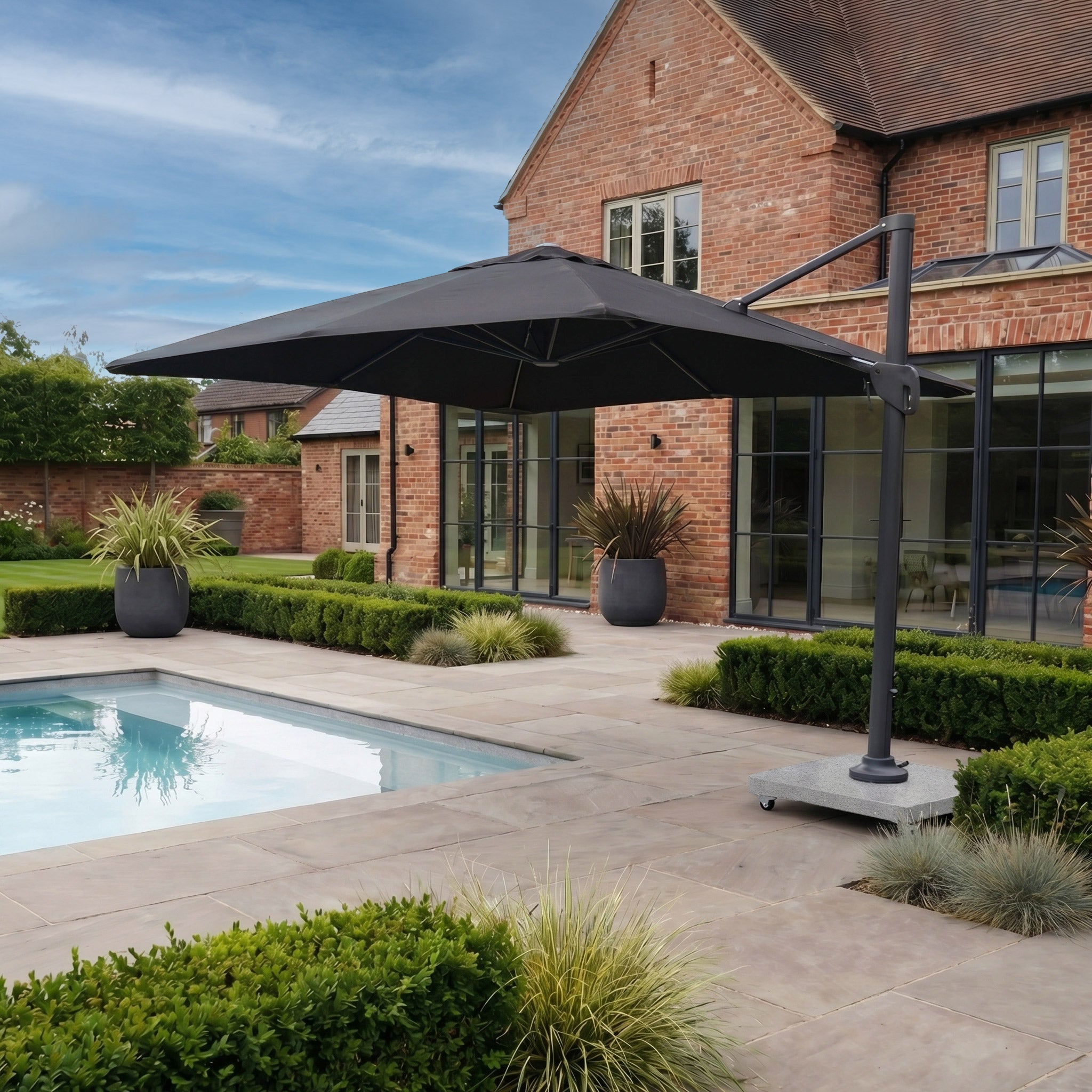 Modern patio featuring the Nexus T2 Premium 3m Square Cantilever Parasol in Black with Salerno 90kg Granite Base, offering 360-degree rotation, positioned beside a small pool, brick house, and neatly trimmed hedges.