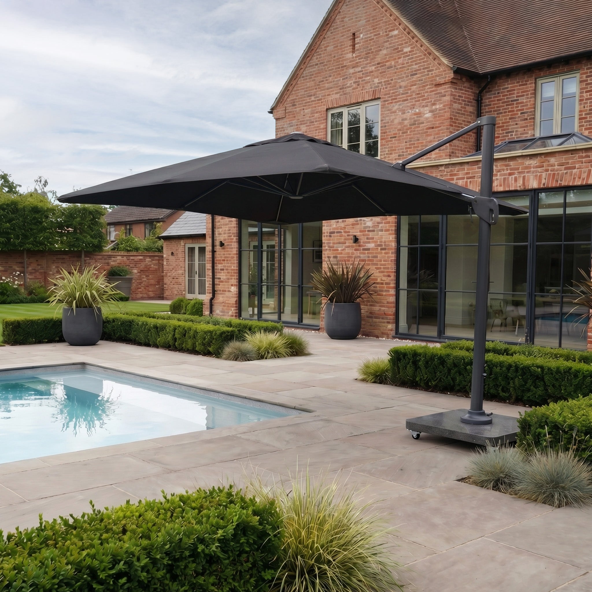 A modern backyard patio with pool and lush plants features the Nexus T2 Premium 3m Square Cantilever Parasol in Black with a 90kg granite base, offering 360-degree rotation for versatile shade.